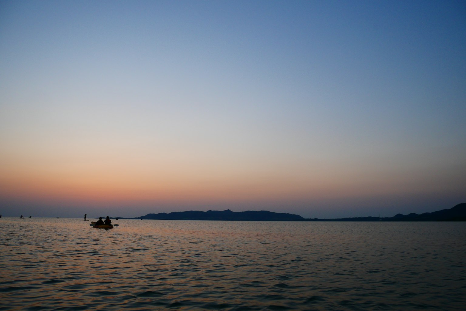 A tranquil sea with a sunset and a small boat floating