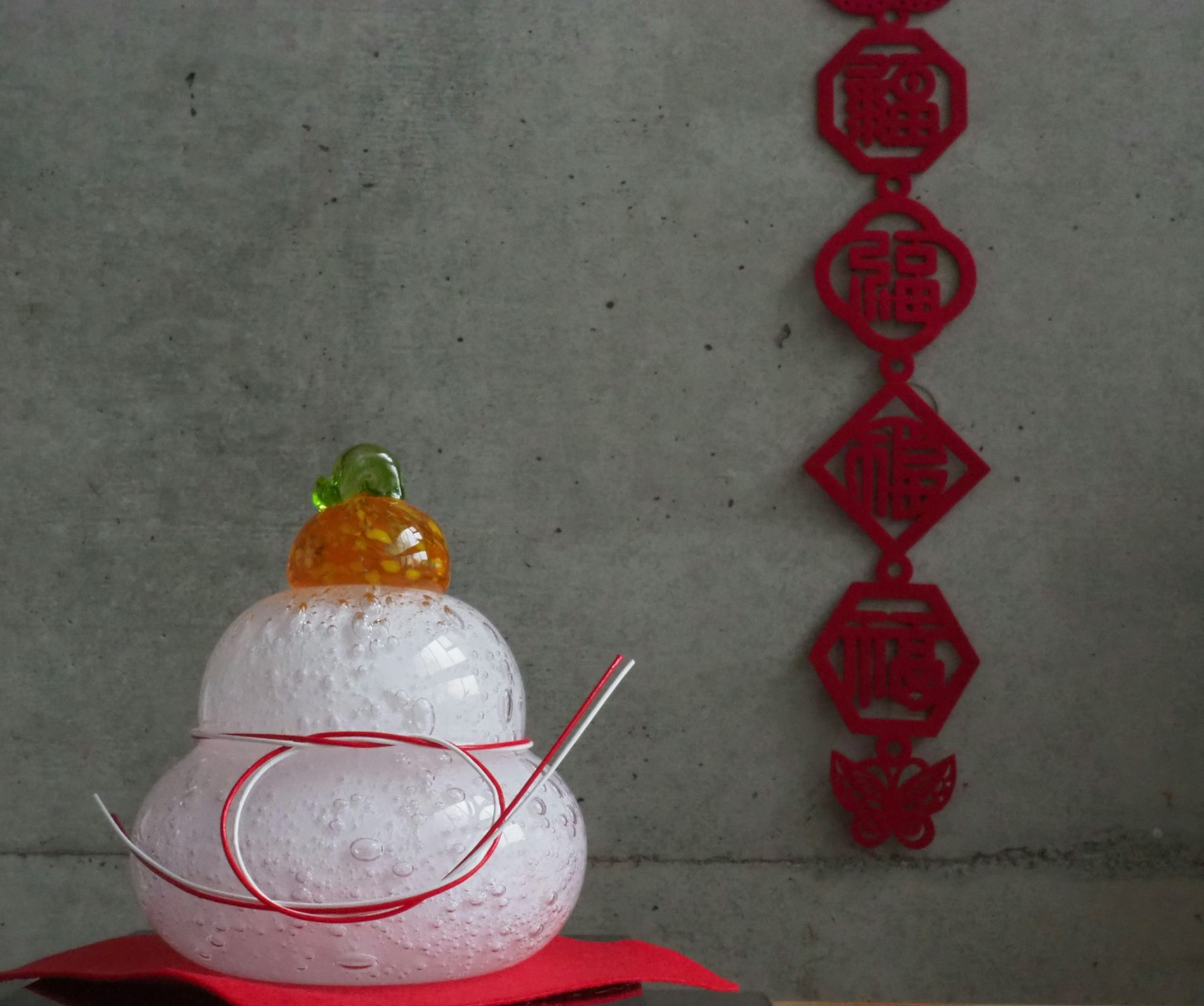 A decorative white round object topped with orange and green ornaments with red decorations in the background