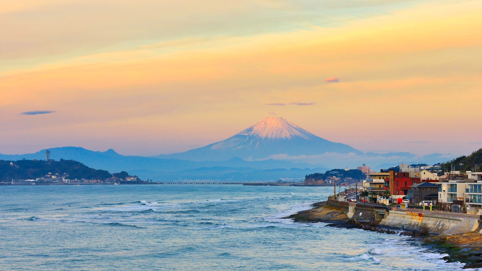 Vue pittoresque du mont Fuji au coucher du soleil avec des bâtiments côtiers et des vagues océaniques