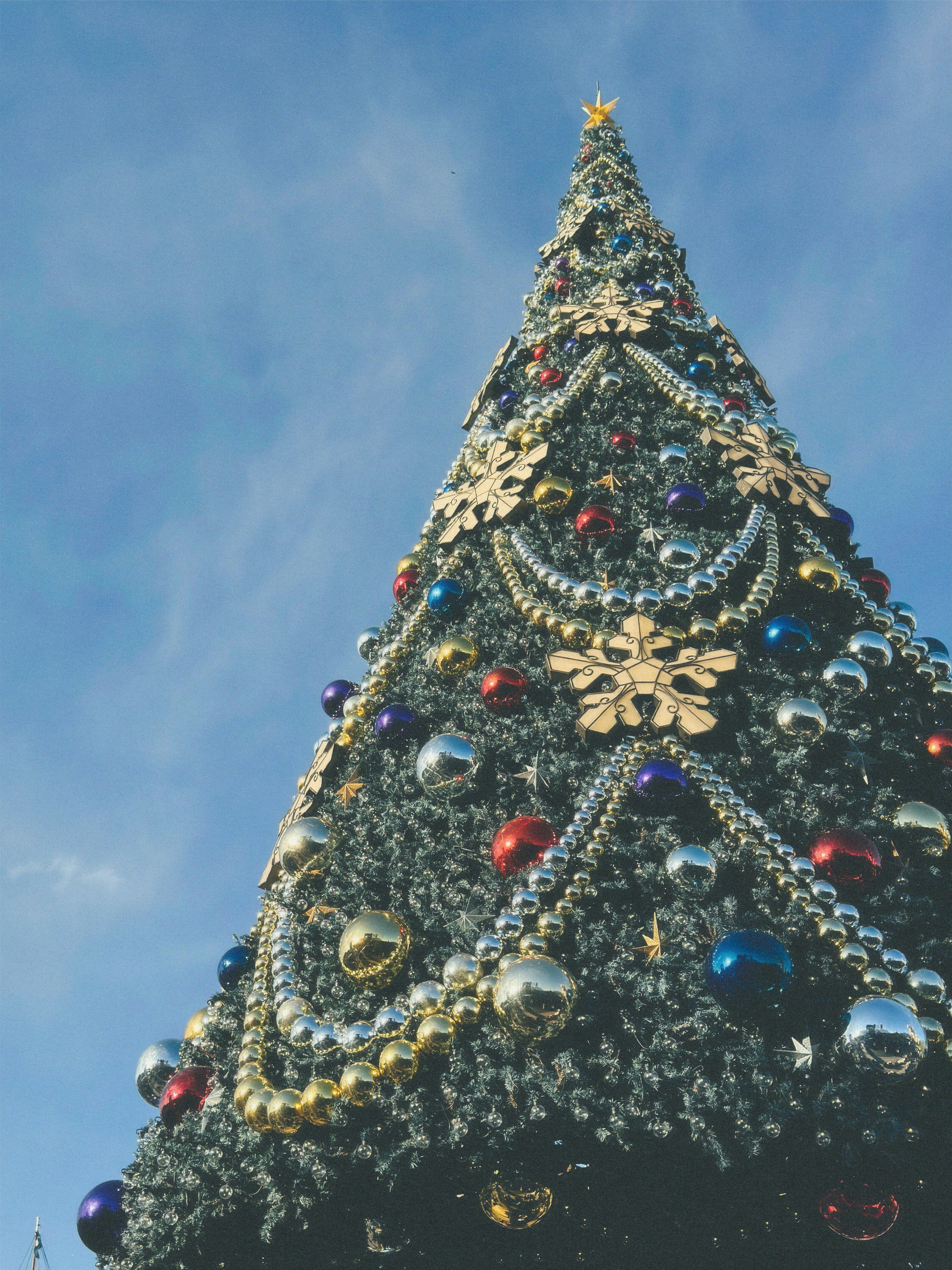 Un arbre de Noël vibrant orné de flocons de neige dorés et d'ornements colorés sous un ciel bleu