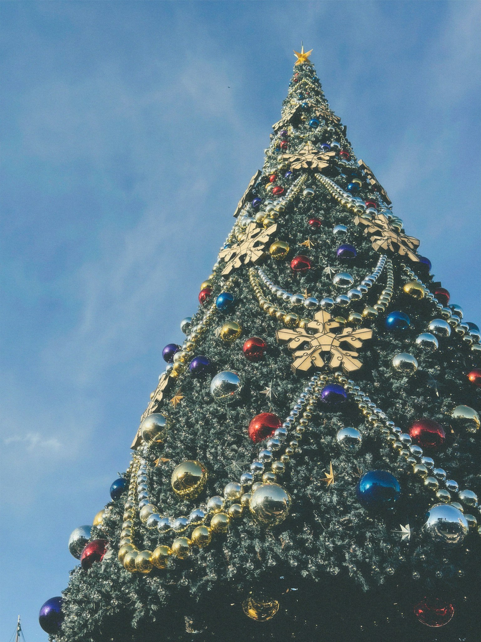 Pohon Natal yang cerah dihiasi dengan bunga salju emas dan ornamen berwarna-warni di bawah langit biru