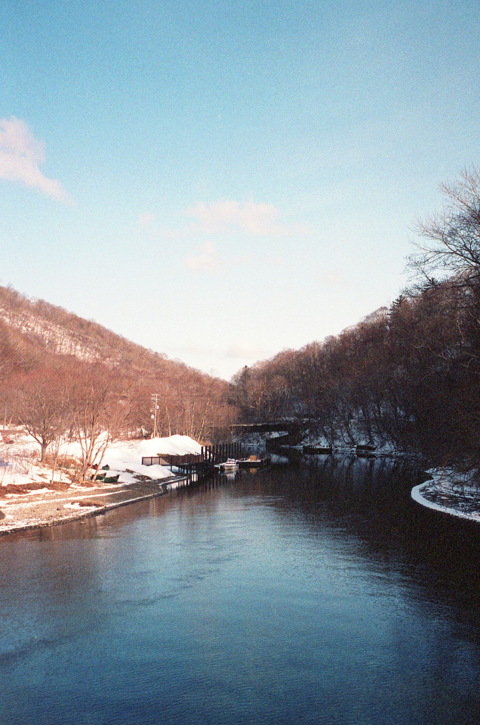 Winter landscape featuring a river surrounded by snow-covered mountains and clear blue sky