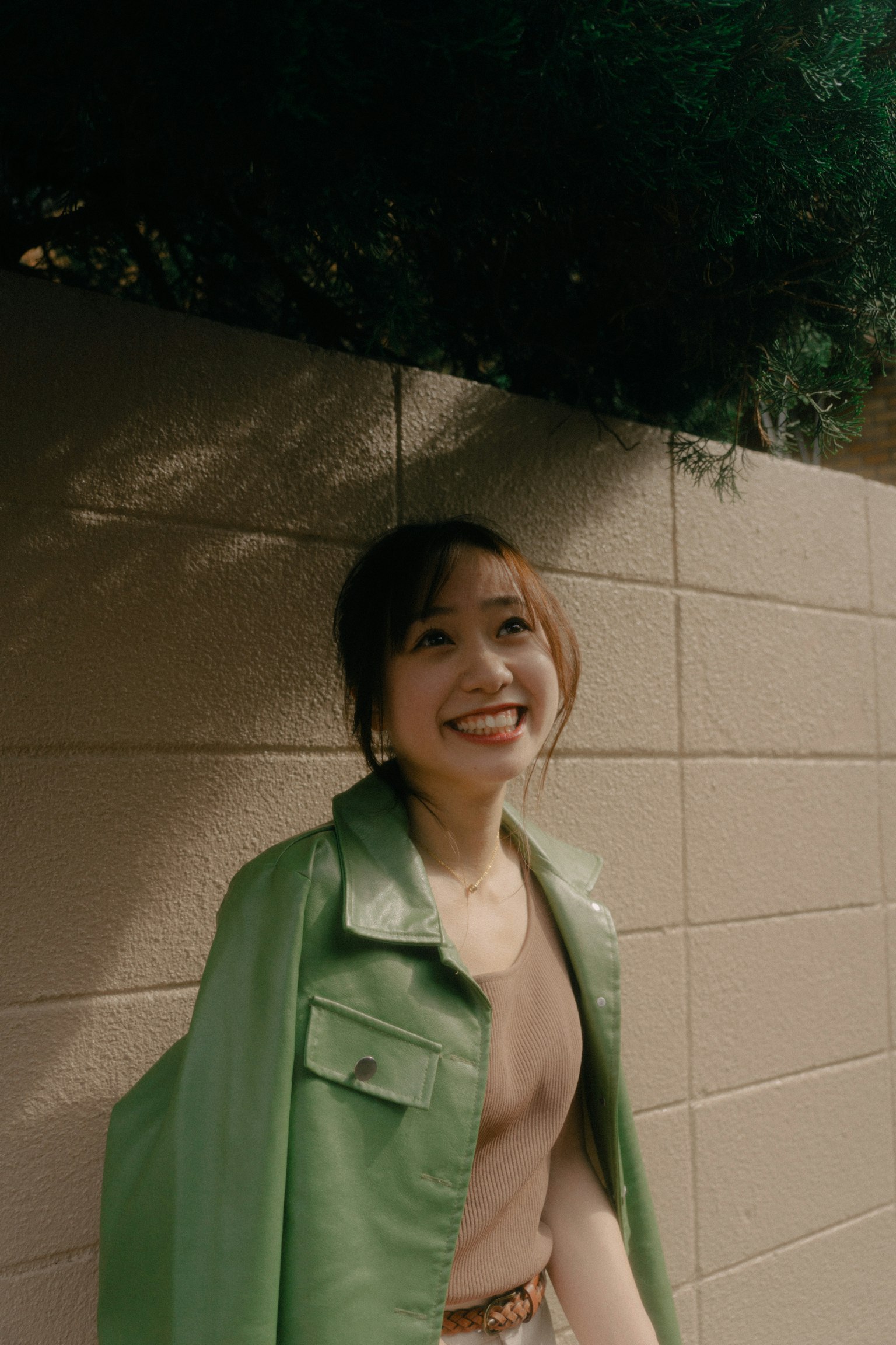 穿着绿色夹克的女性在墙前微笑