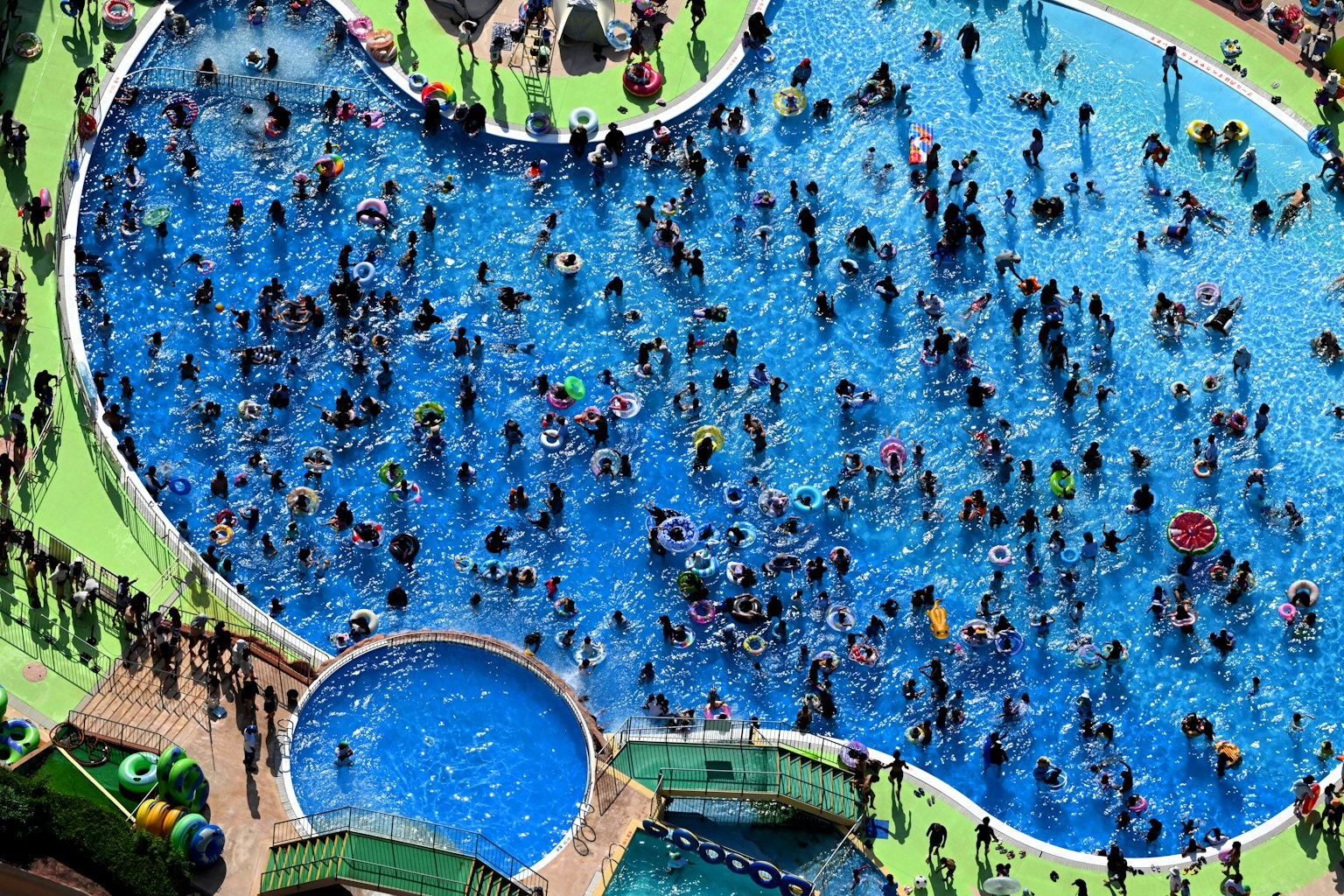 Crowd of people swimming in a blue pool with colorful floaties