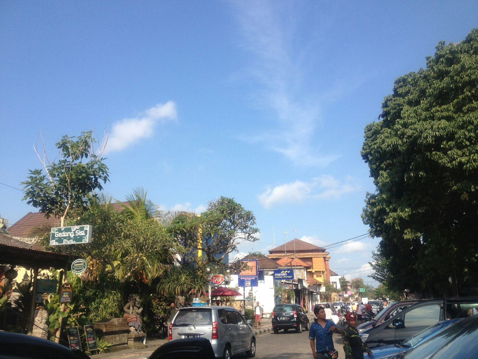 Cảnh đường phố ở Bali với bầu trời xanh và cây cối xe đỗ và cửa hàng địa phương