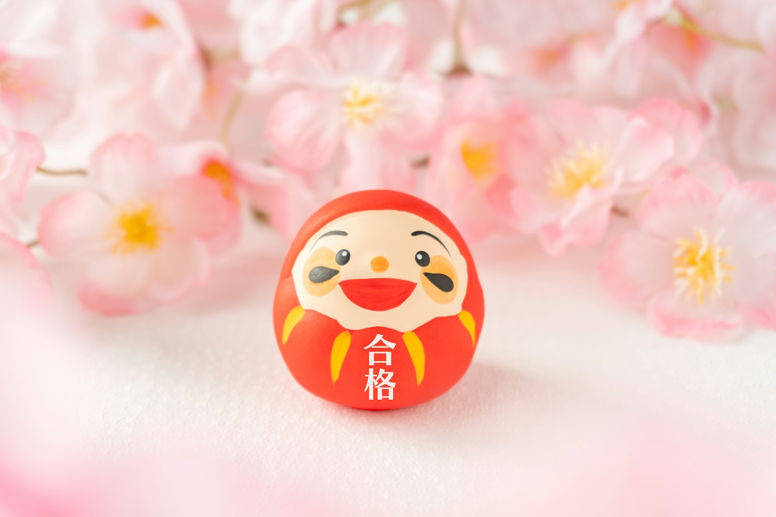 Muñeca daruma roja colocada frente a flores de cerezo