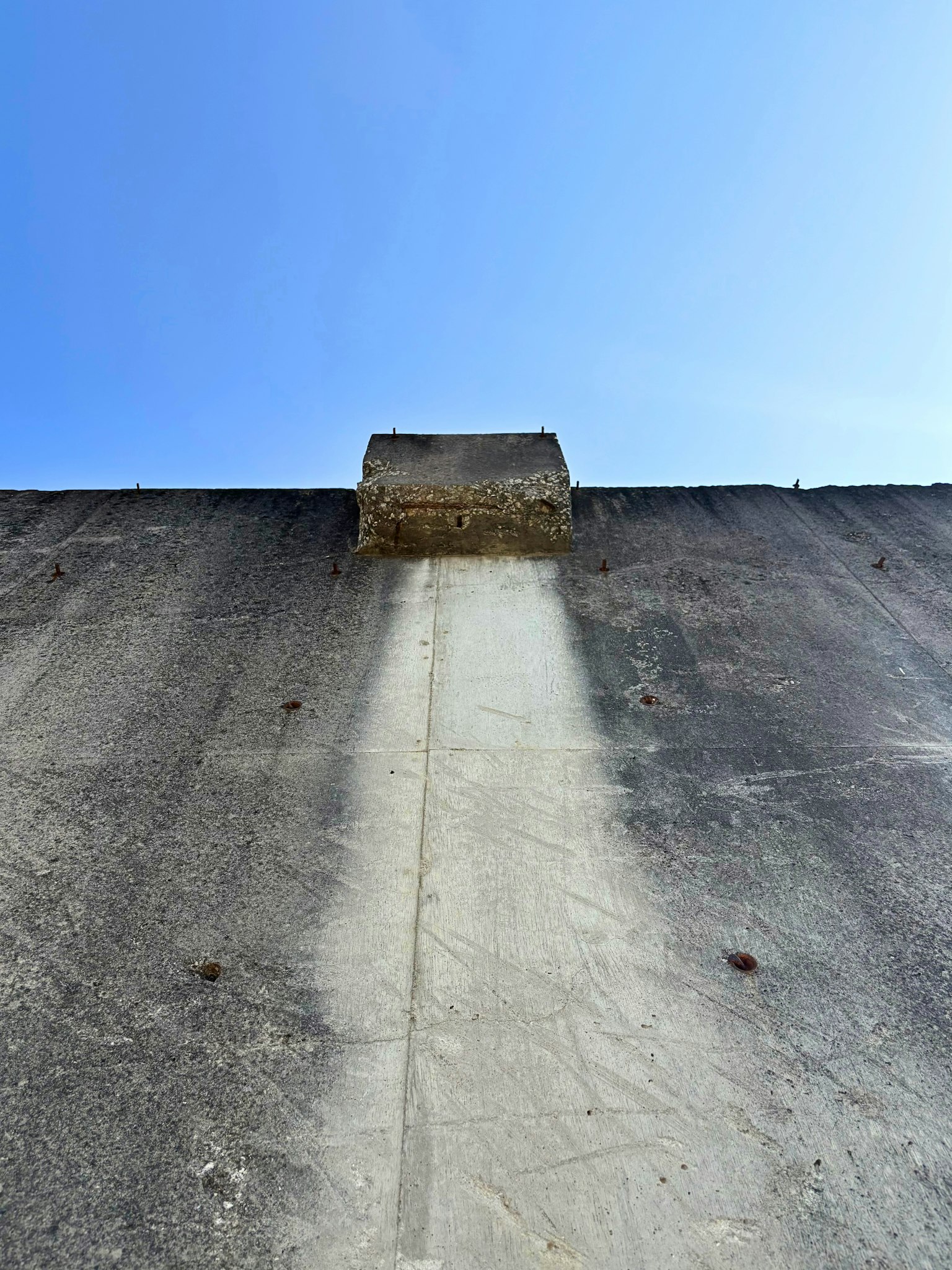 Betonwand unter einem blauen Himmel mit einer kleinen Struktur oben