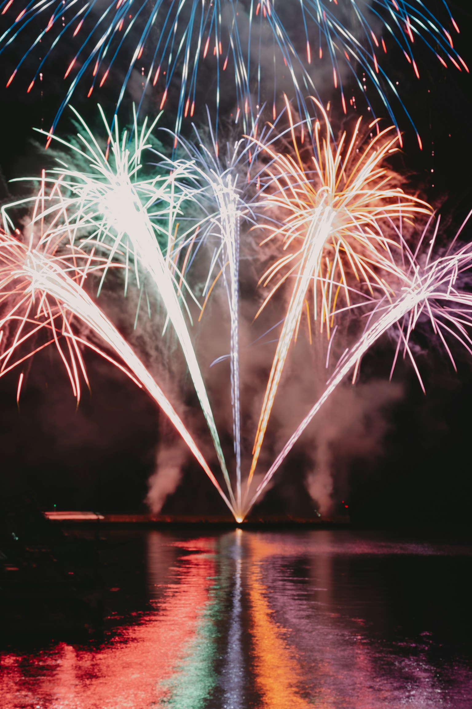 Fuegos artificiales coloridos estallando en el cielo nocturno reflejándose en el agua