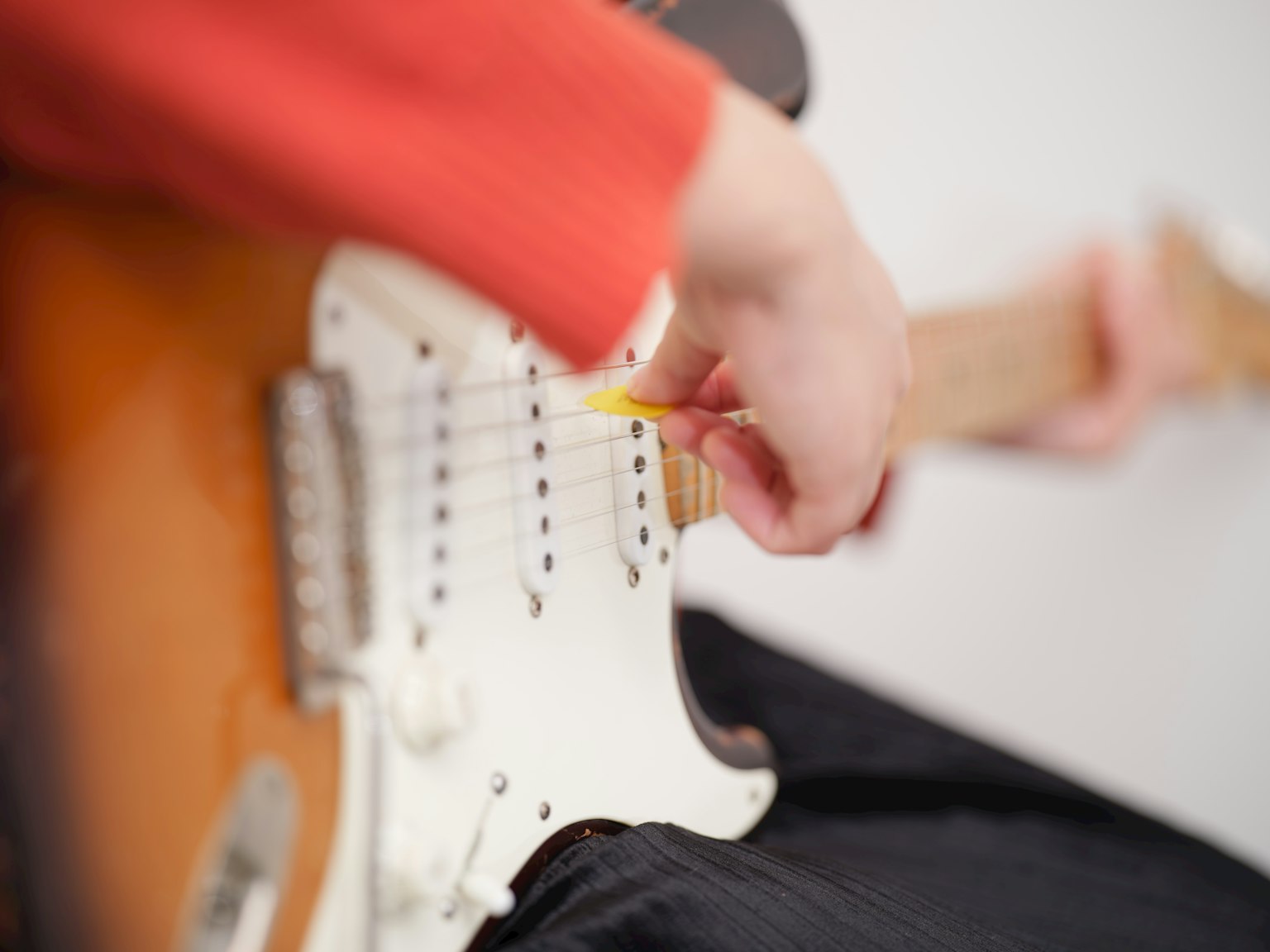 Orang yang mengenakan sweter oranye sedang bermain gitar Stratocaster