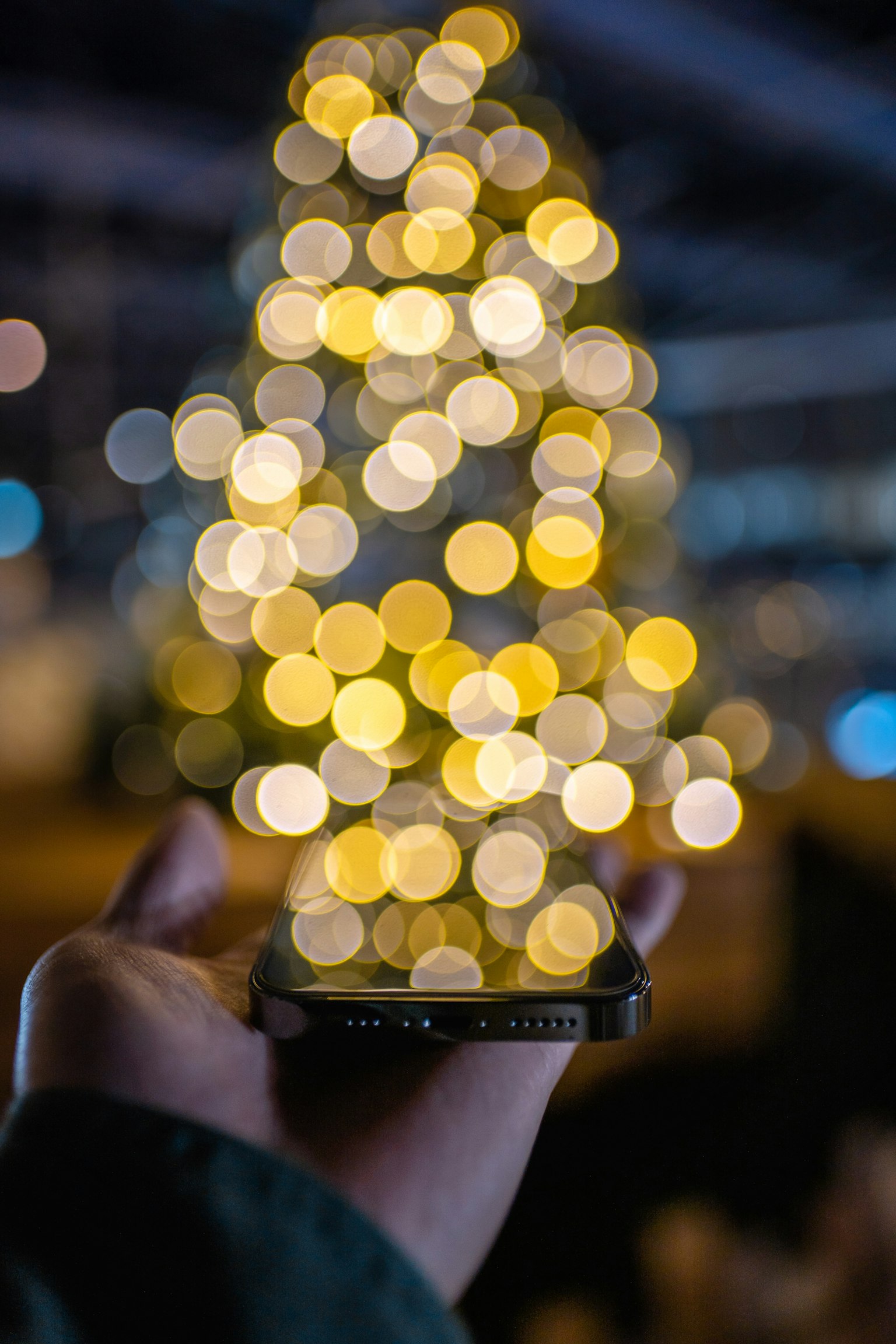 Un smartphone tenu dans une main avec un arbre de Noël flou en arrière-plan