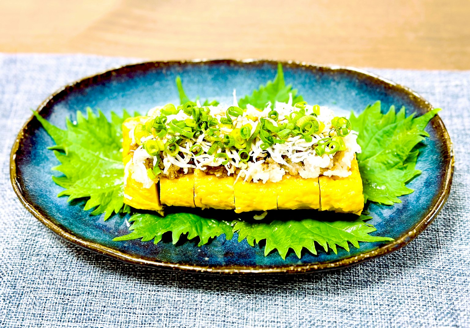 Japanisches Omelett garniert mit kleinen Fischen und Frühlingszwiebeln auf einem blauen Teller