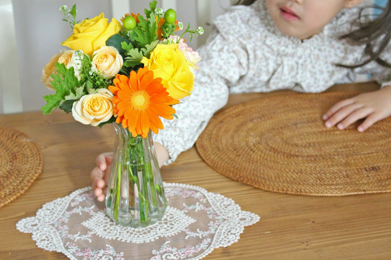 Một đứa trẻ với tay tới một bình hoa nhiều màu trên bàn gỗ
