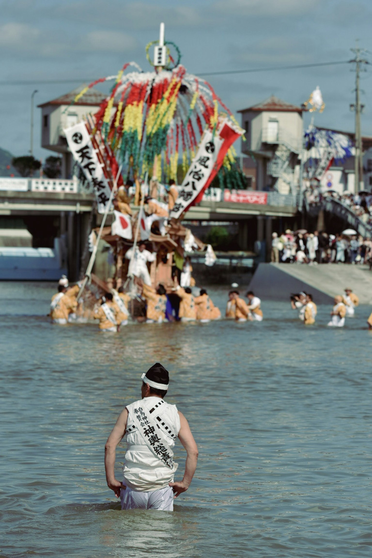 川で祭りを楽しむ人々と色とりどりの飾りを持つ山車