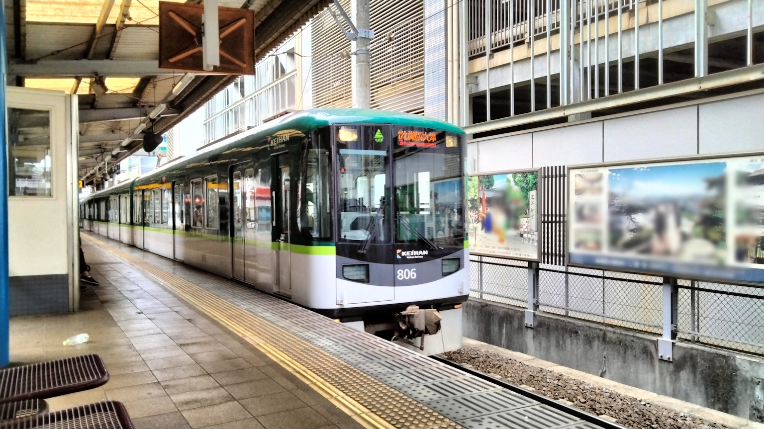 รถไฟสีเขียวและขาวจอดอยู่ที่สถานีมีม้านั่งใกล้เคียงและอาคารรอบข้าง