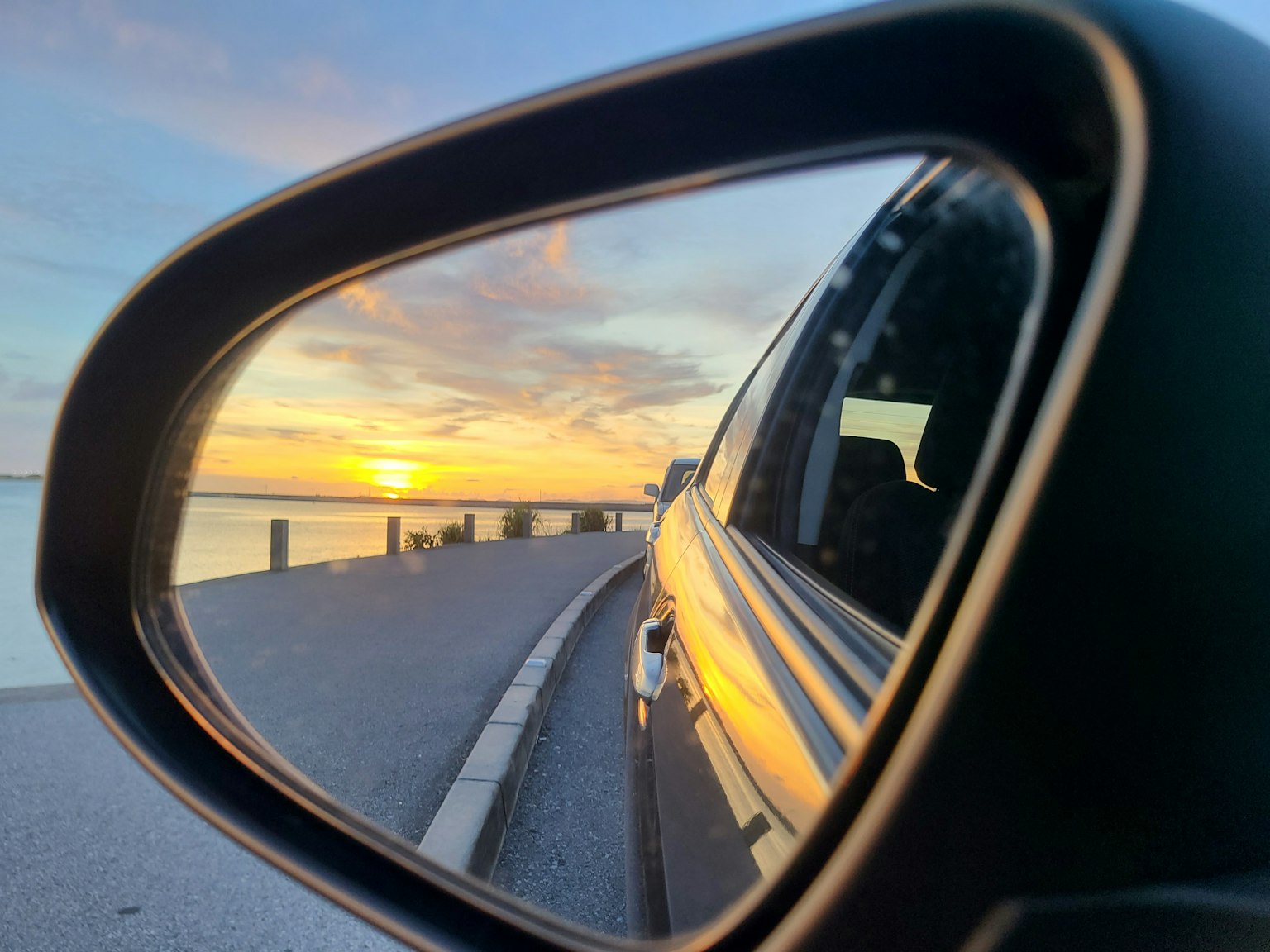 Senja yang dipantulkan di cermin samping mobil dengan jalan pesisir