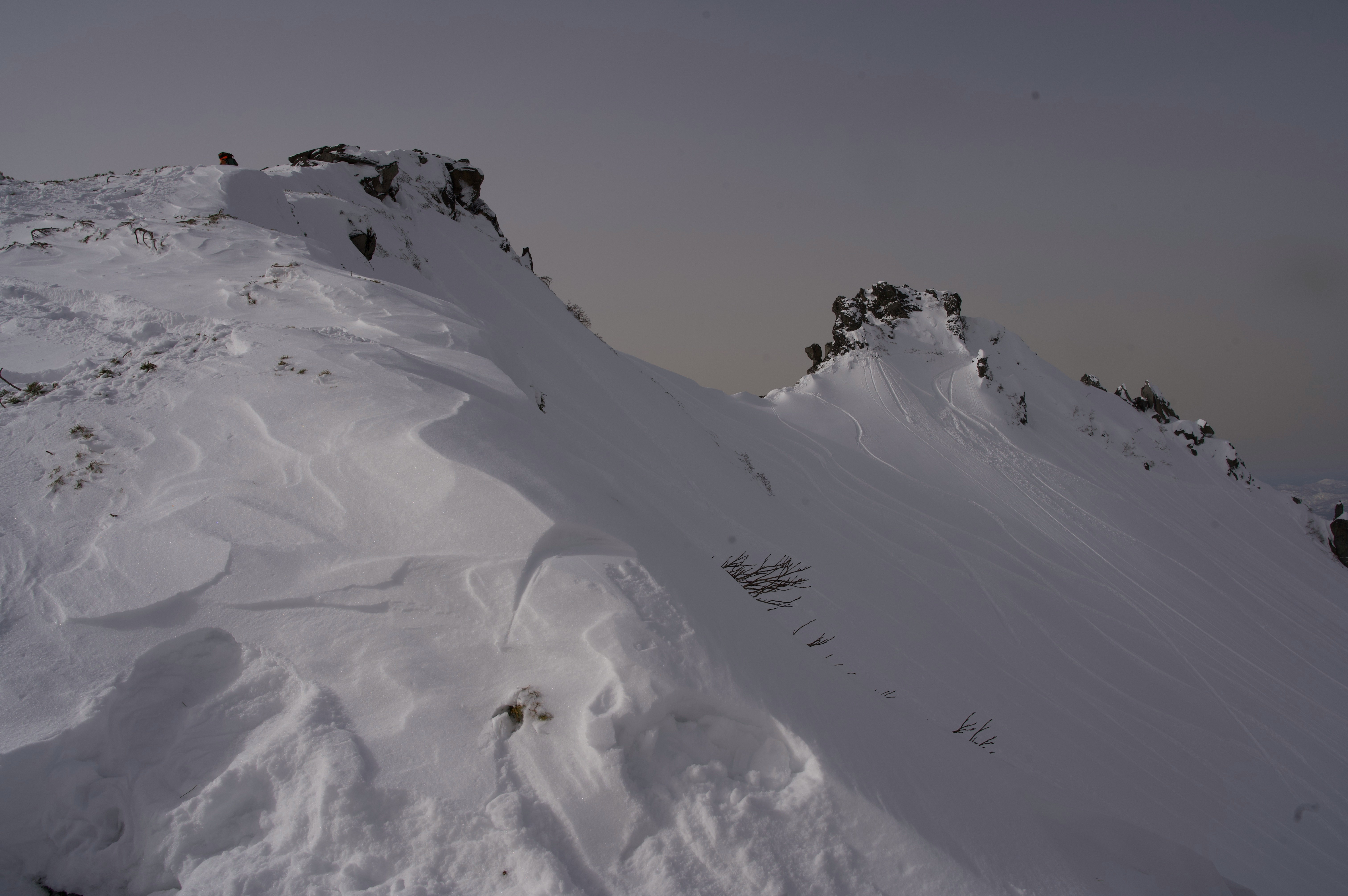 Blick auf eine verschneite Bergpiste mit Skifahrern auf dem Grat