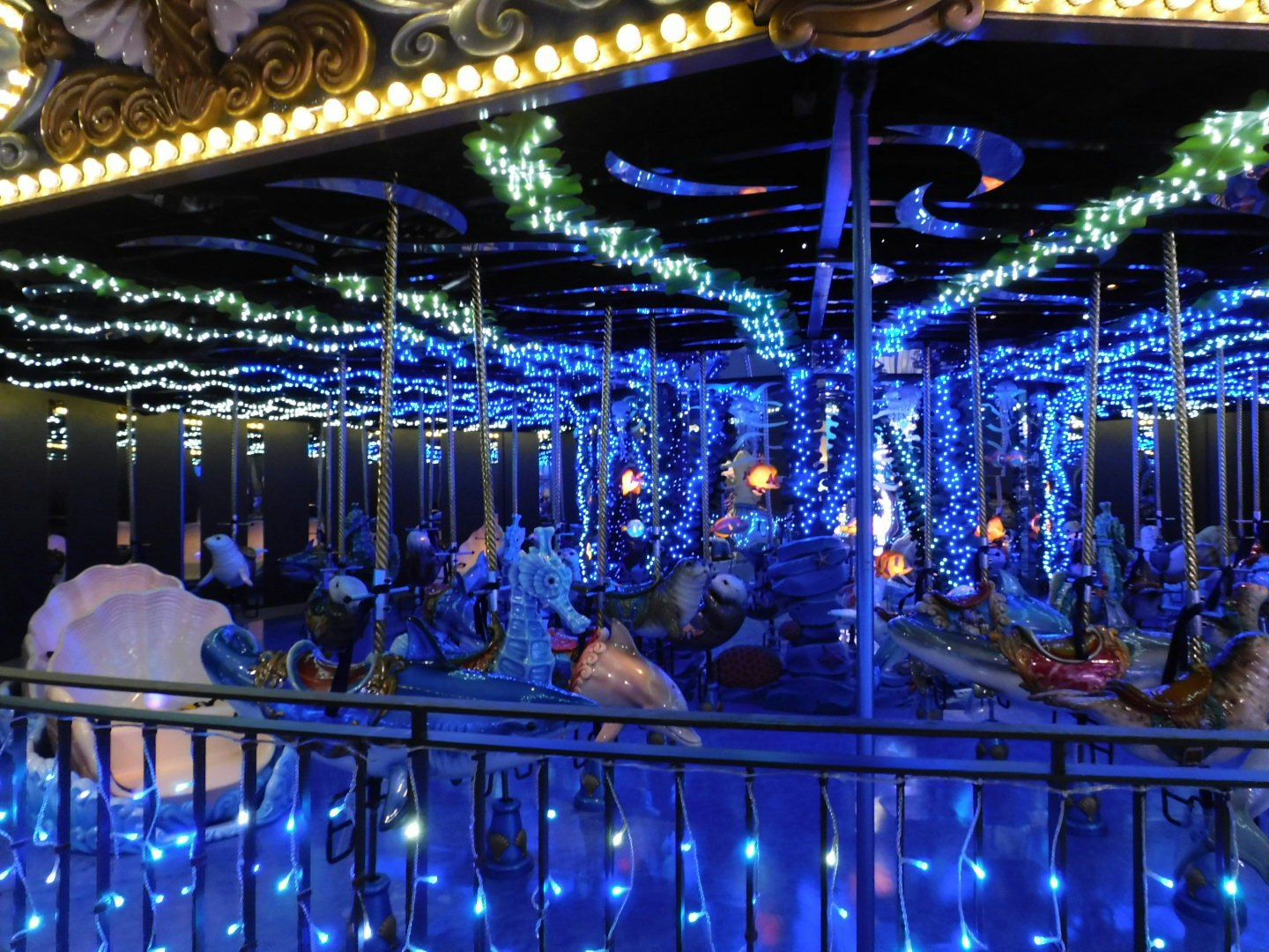 青いイルミネーションの回廊で人々が集う夜の遊園地