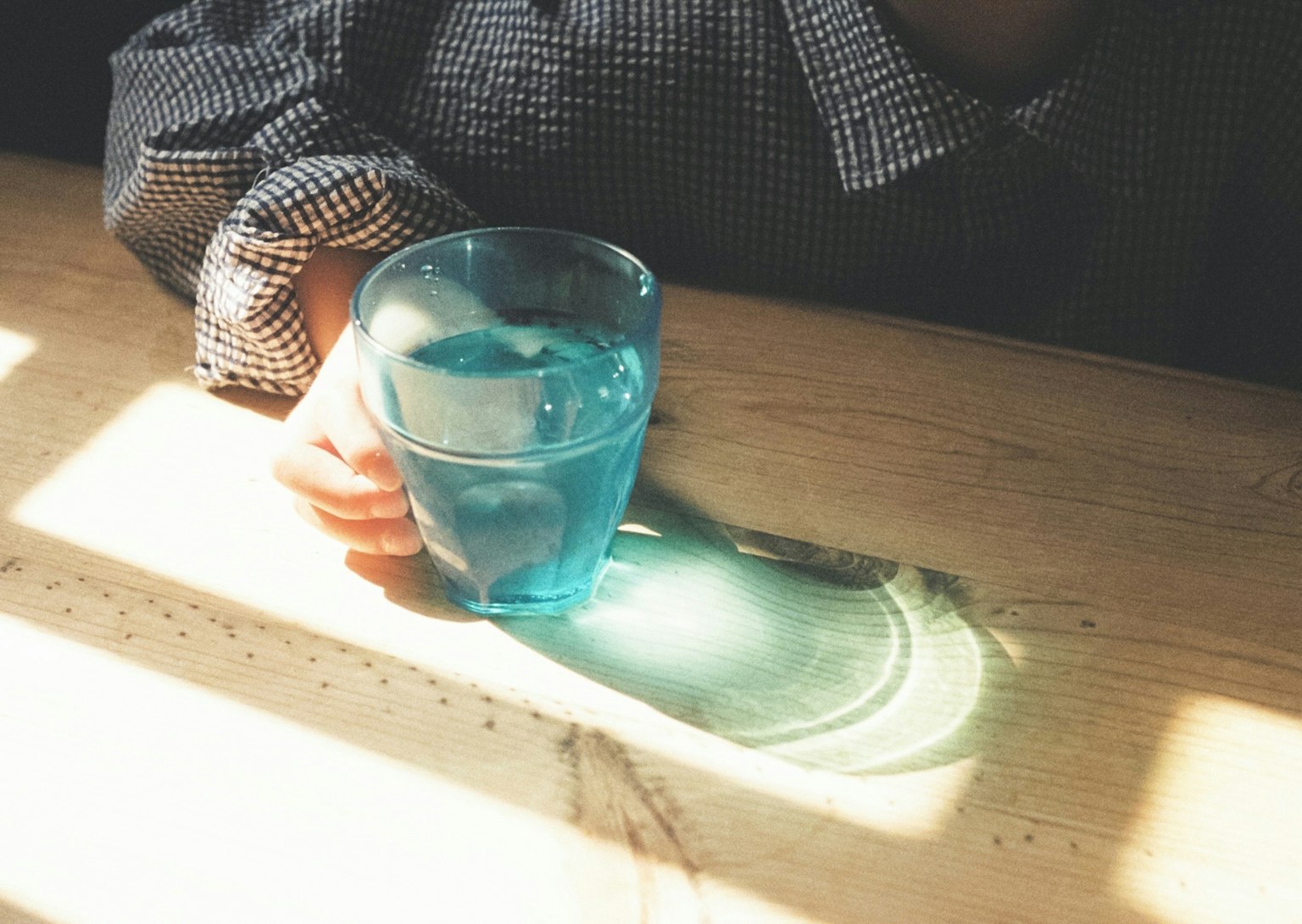 手握着蓝色玻璃杯，木桌上有光的反射