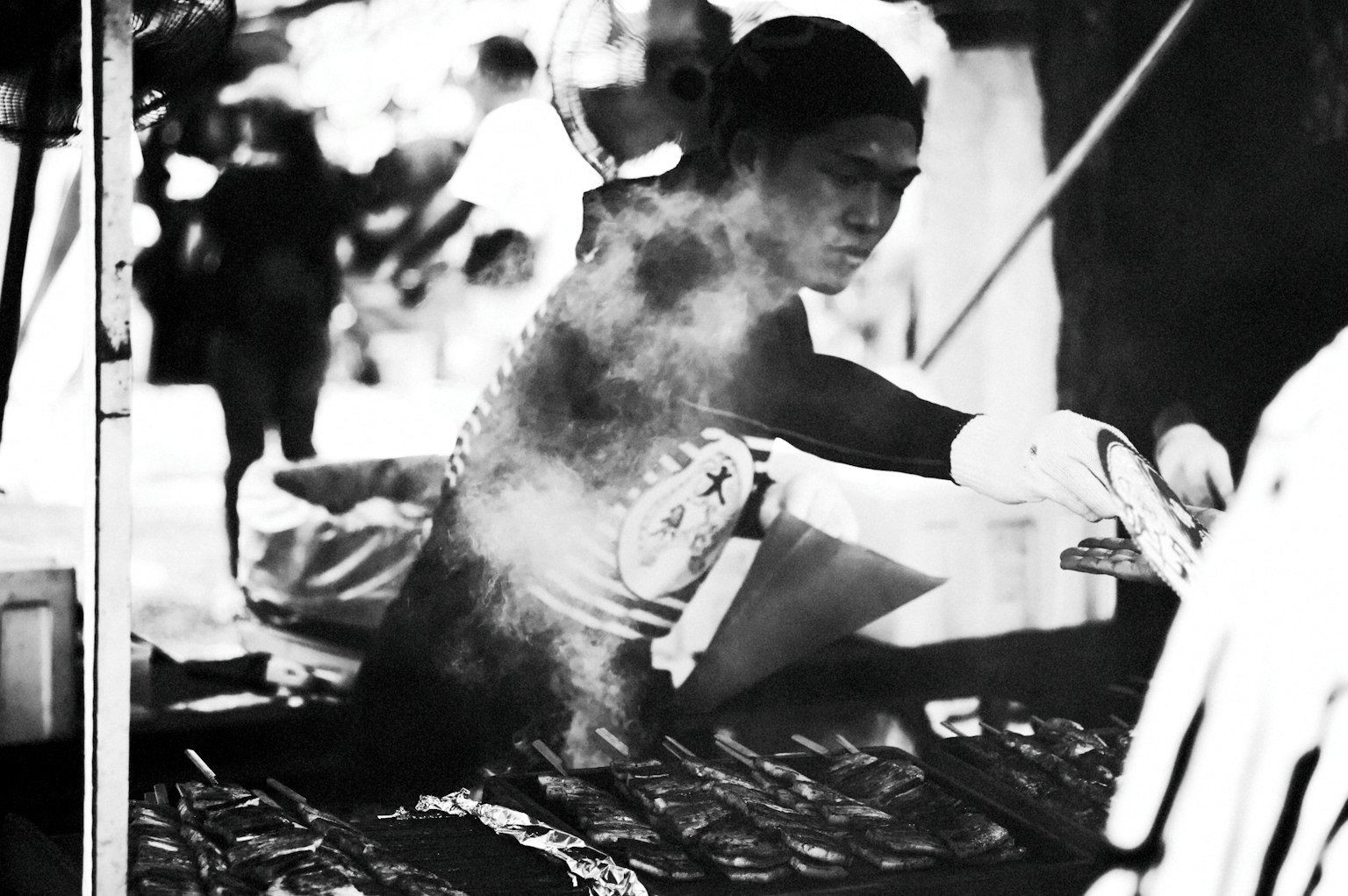 Foto in bianco e nero di un cuoco che griglia pesce in un chiosco di cibo