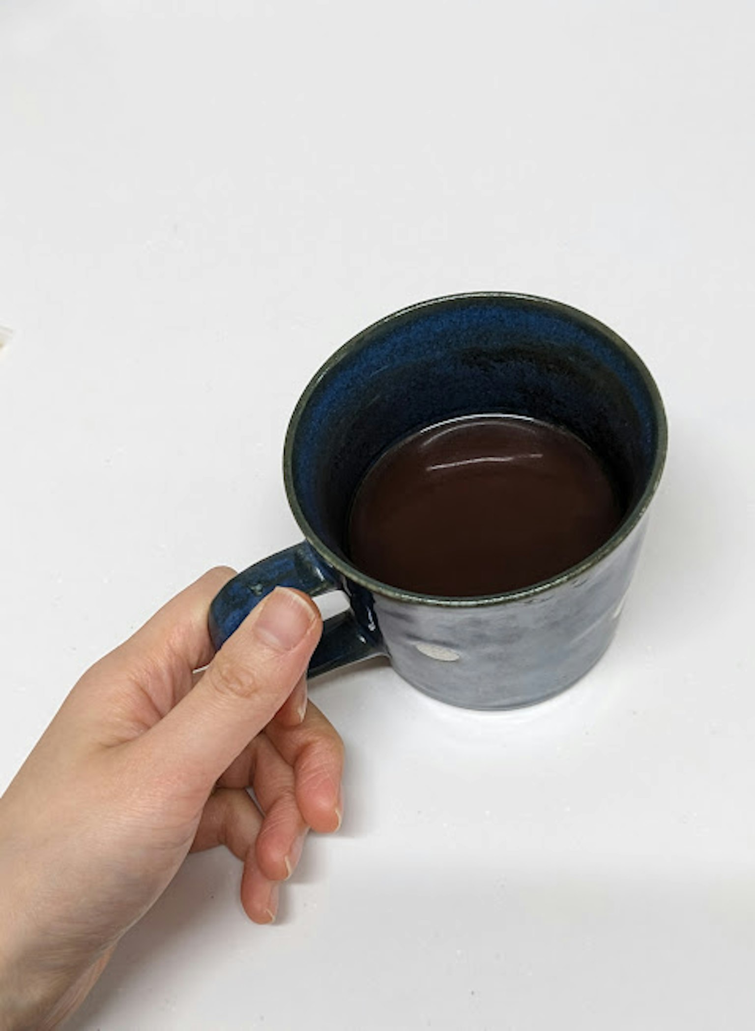 มือถือแก้วกาแฟสีน้ำเงินที่เต็มไปด้วยกาแฟเข้ม