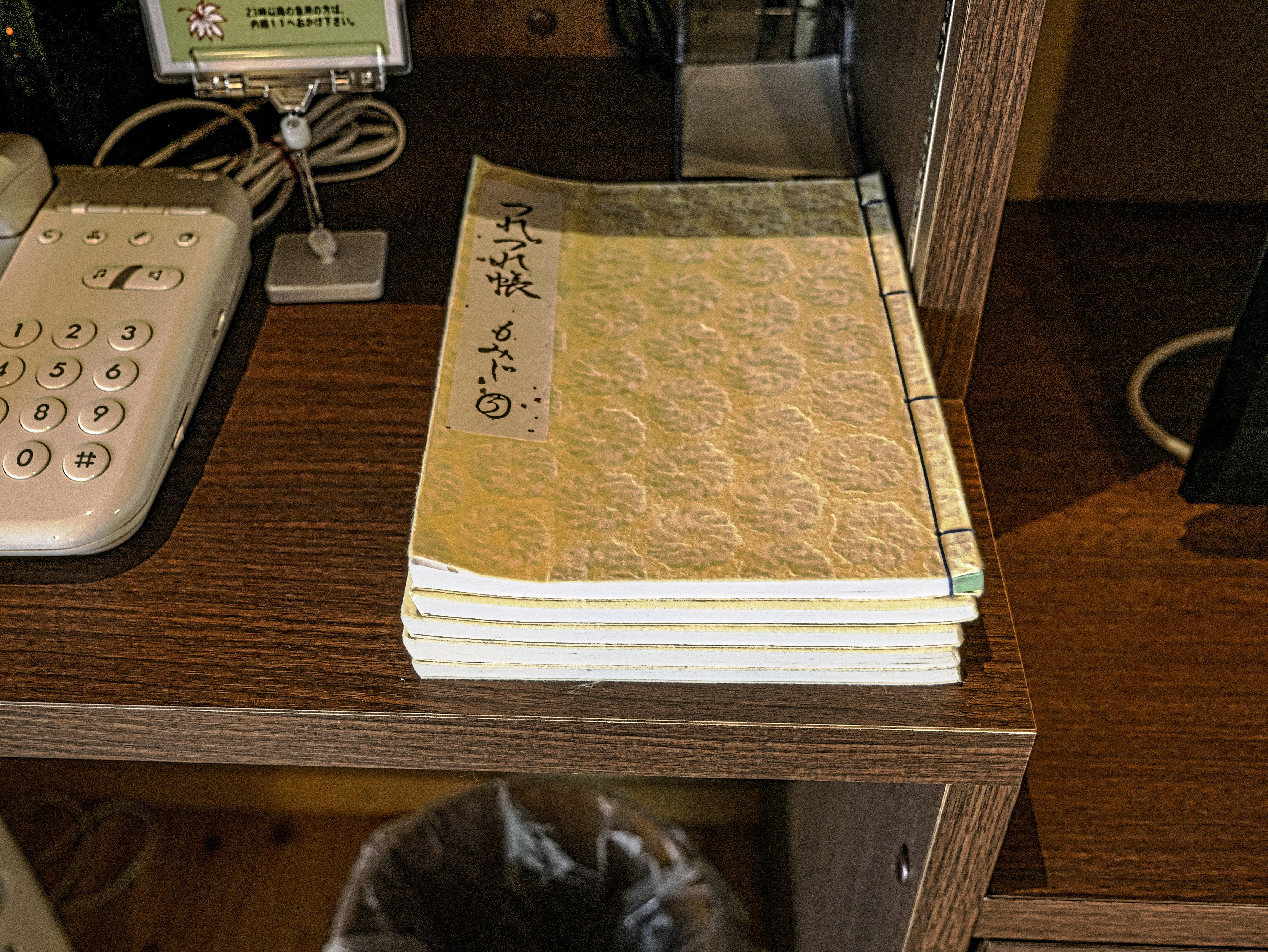 木製の机の上に積まれた和紙の本と電話機