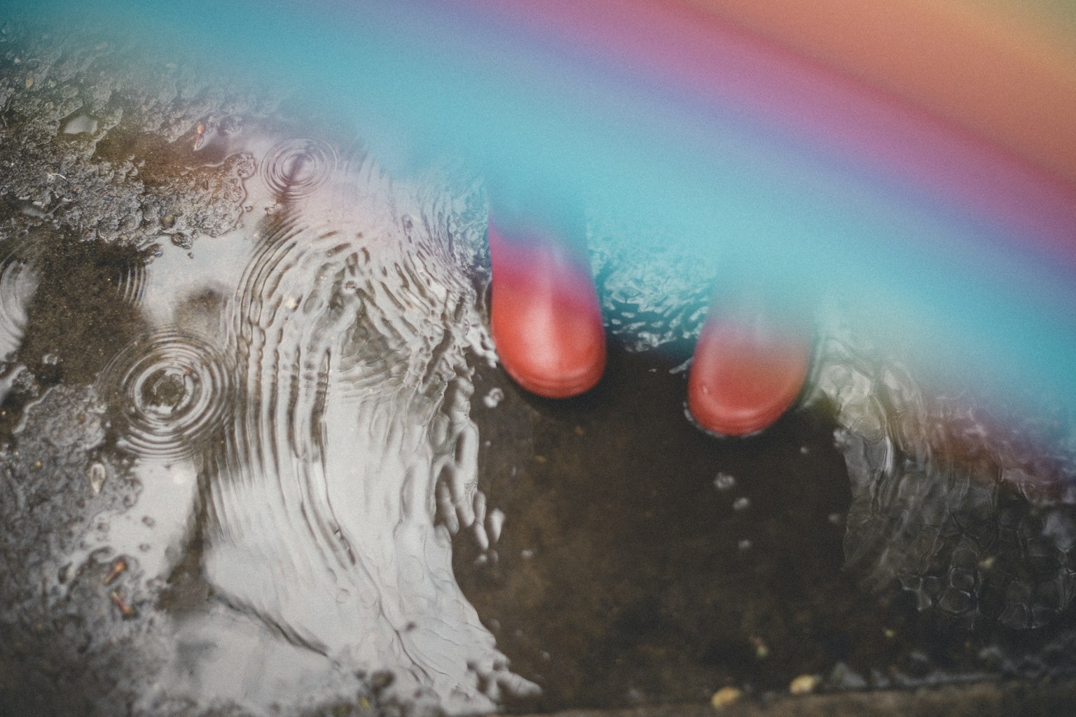 Bottes en caoutchouc rouges dans une flaque d'eau avec un arc-en-ciel au-dessus