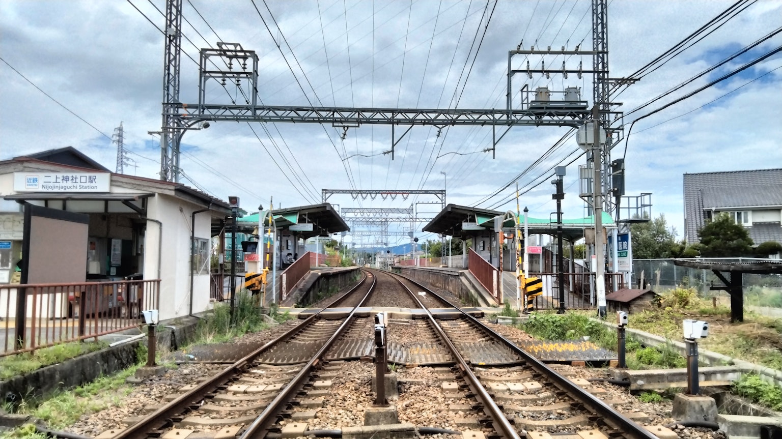 ทัศนียภาพของสถานีรถไฟที่มีรางรถไฟและสัญญาณอาคารใกล้เคียงและท้องฟ้าที่มีเมฆมาก