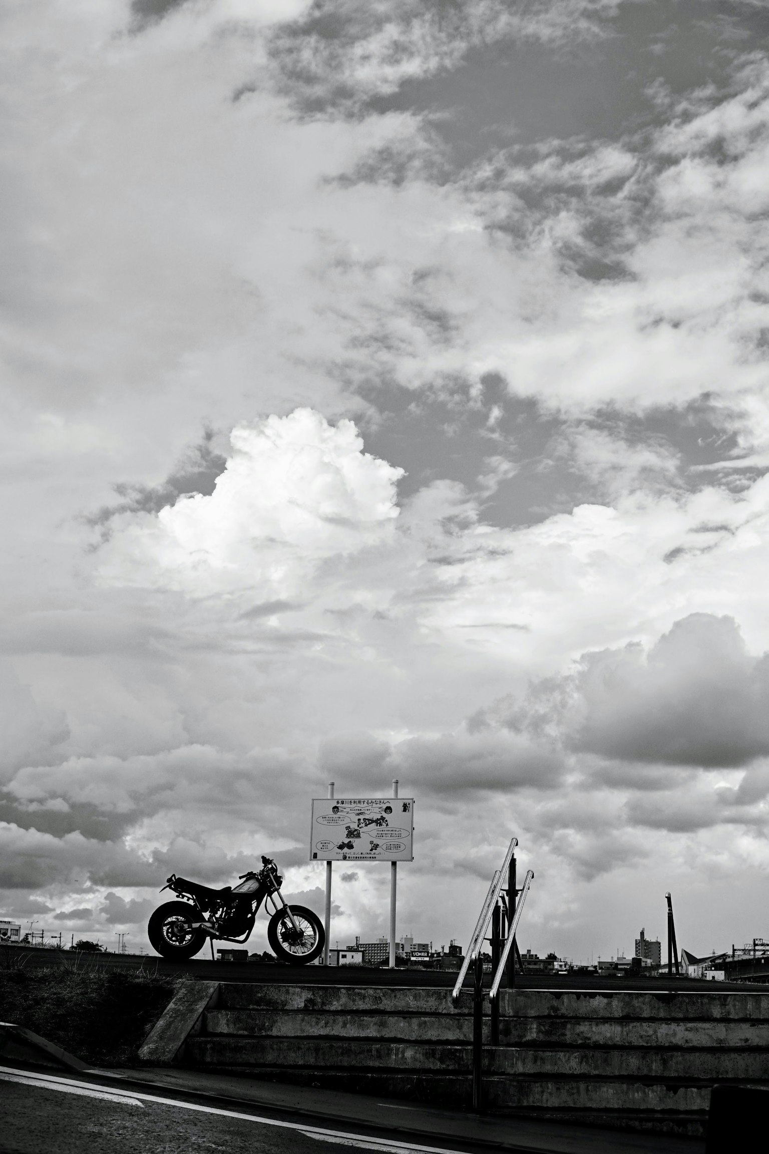 Image en noir et blanc d'une moto garée sous un ciel nuageux
