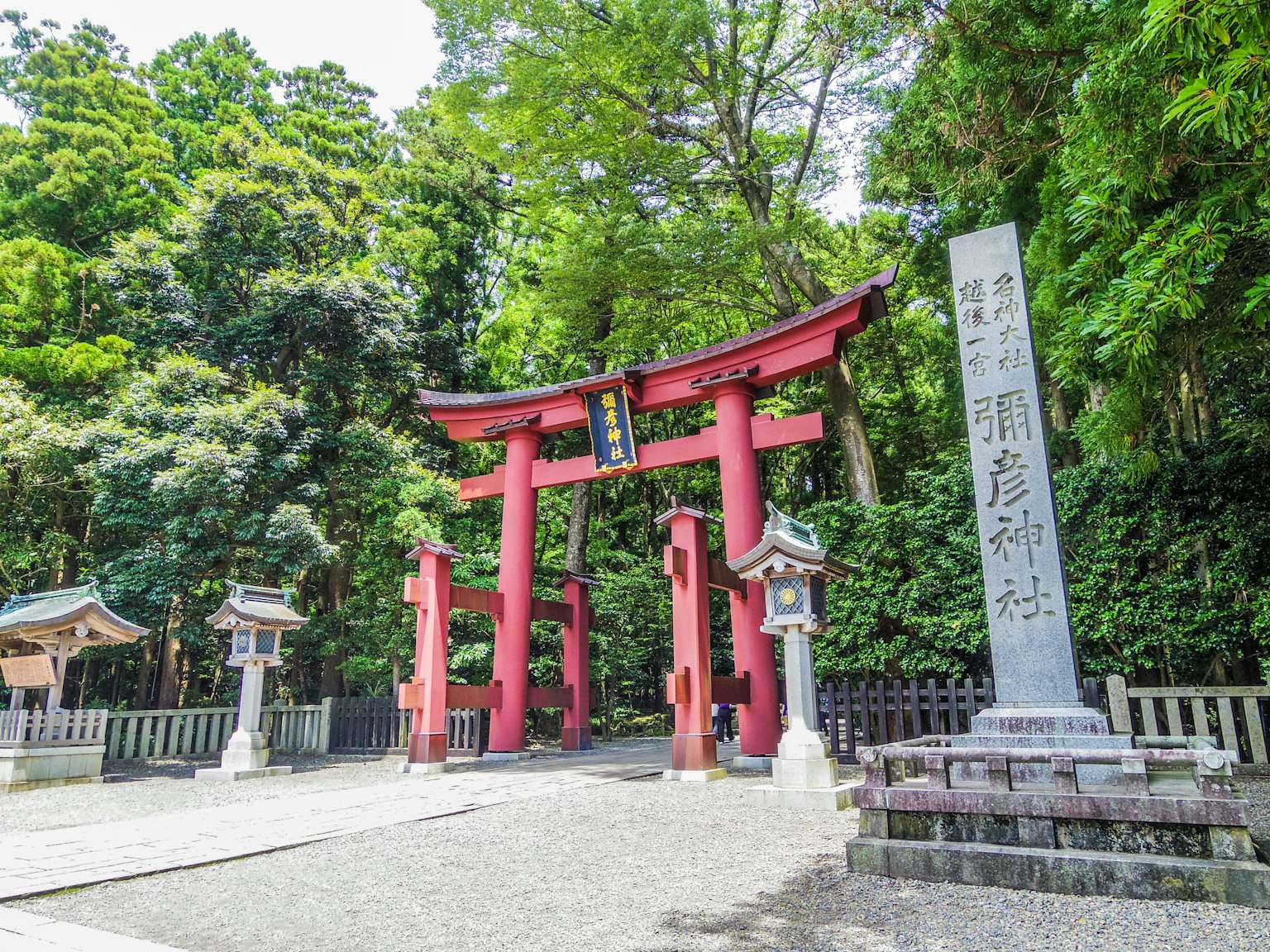 Pintu masuk kuil dengan gerbang torii merah dikelilingi oleh pepohonan hijau lebat