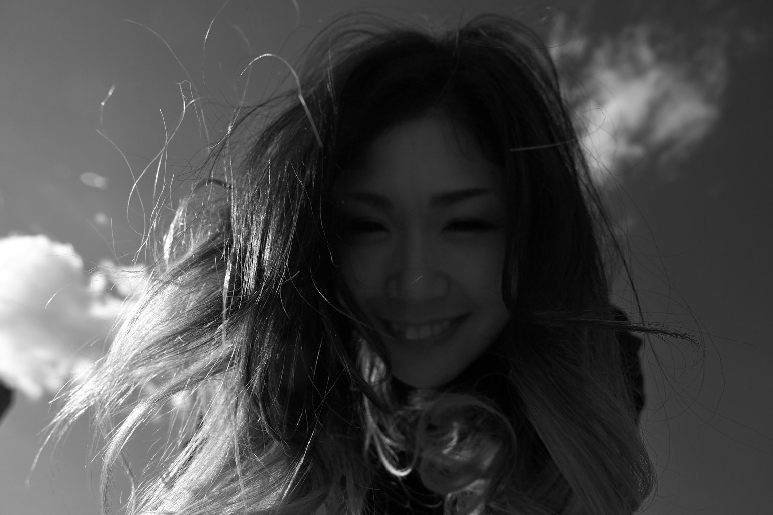 หญิงสาวยิ้มกับผมที่ปลิวในพื้นหลังขาวดำ