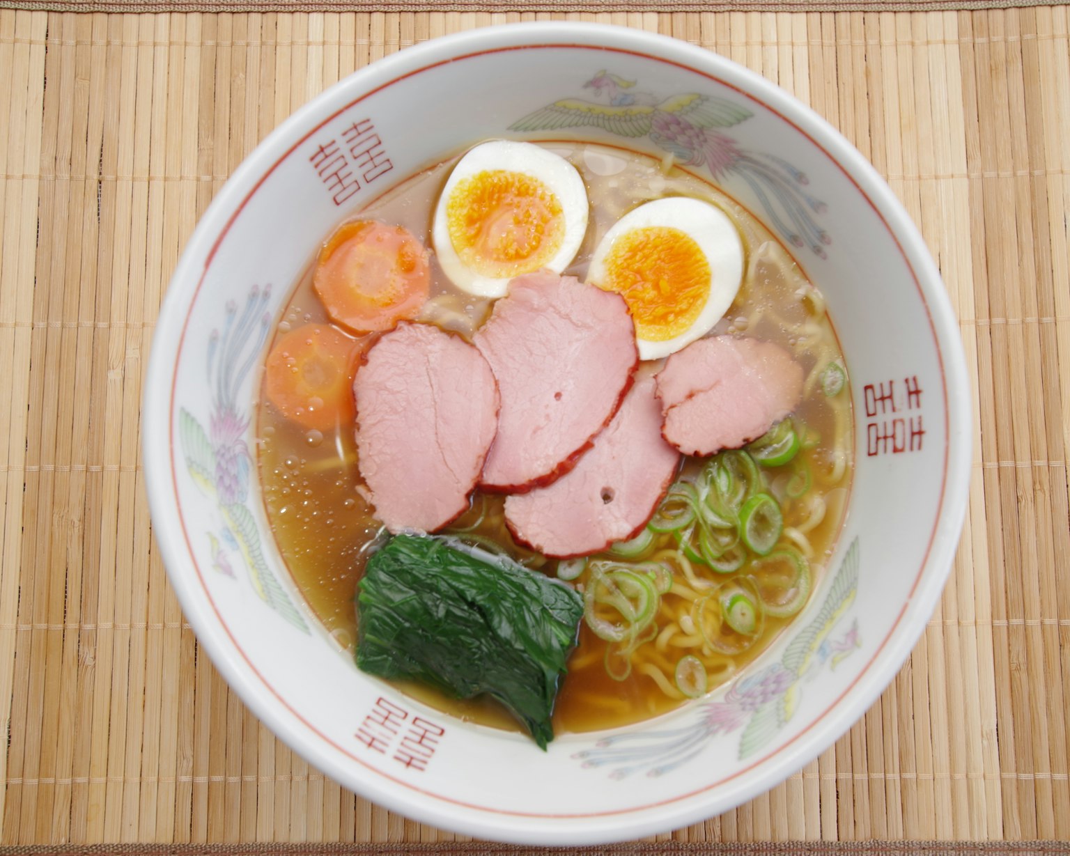 碗装拉面，上面放有切片火腿、煮鸡蛋、胡萝卜、青葱和海藻