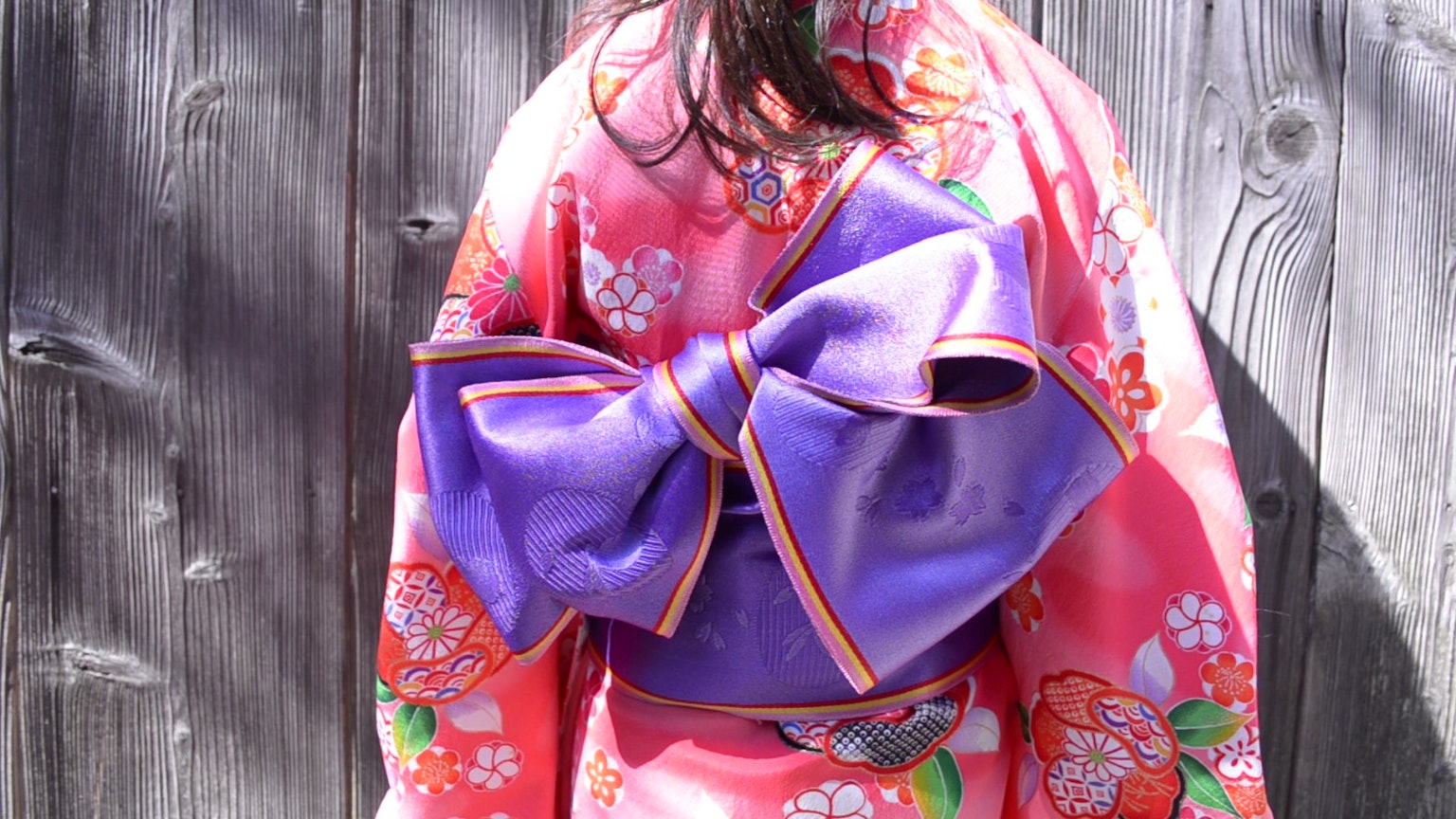Seorang anak mengenakan kimono pink dengan pita ungu besar di belakang