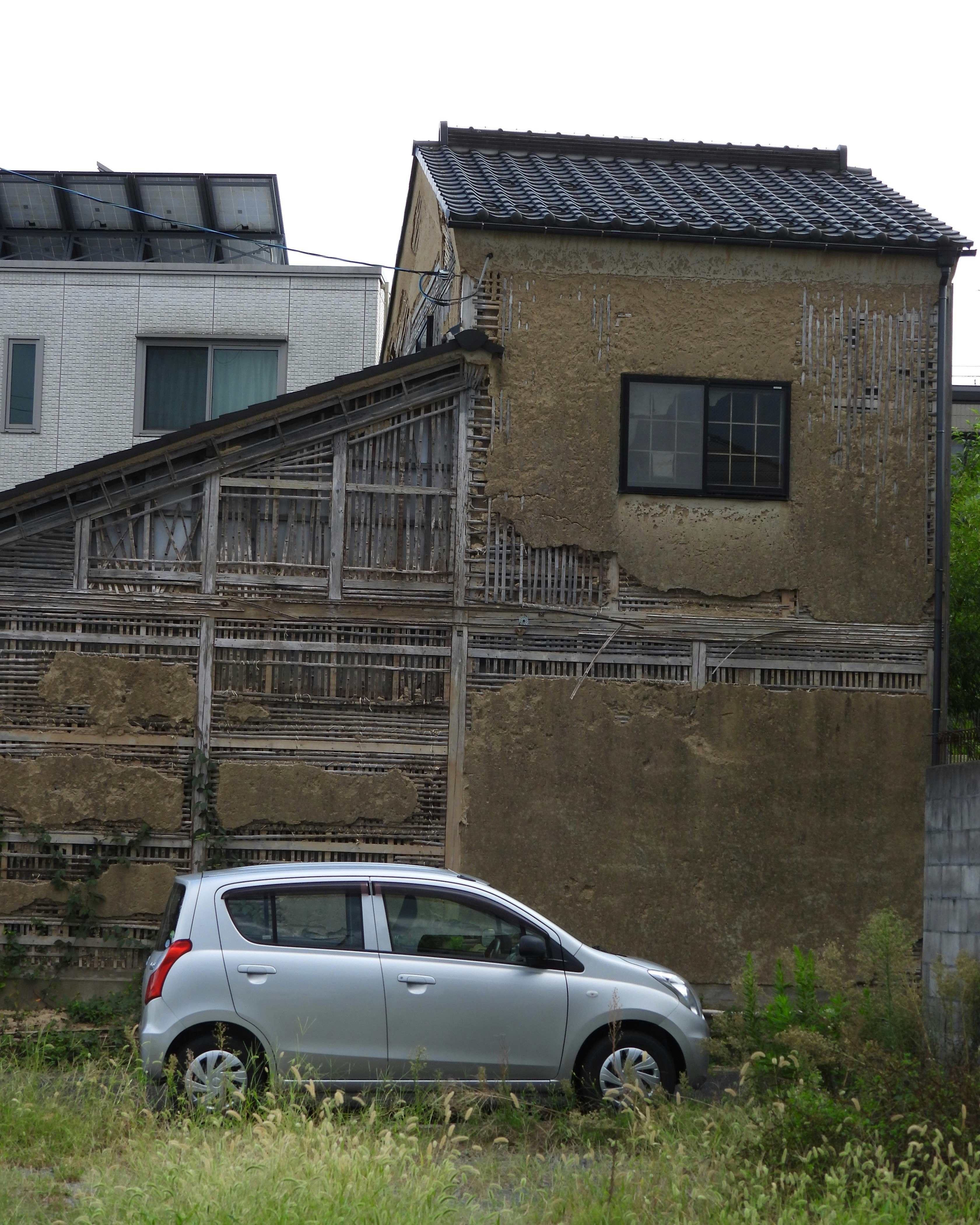 草地に停まるシルバーの車と古い建物のある路地