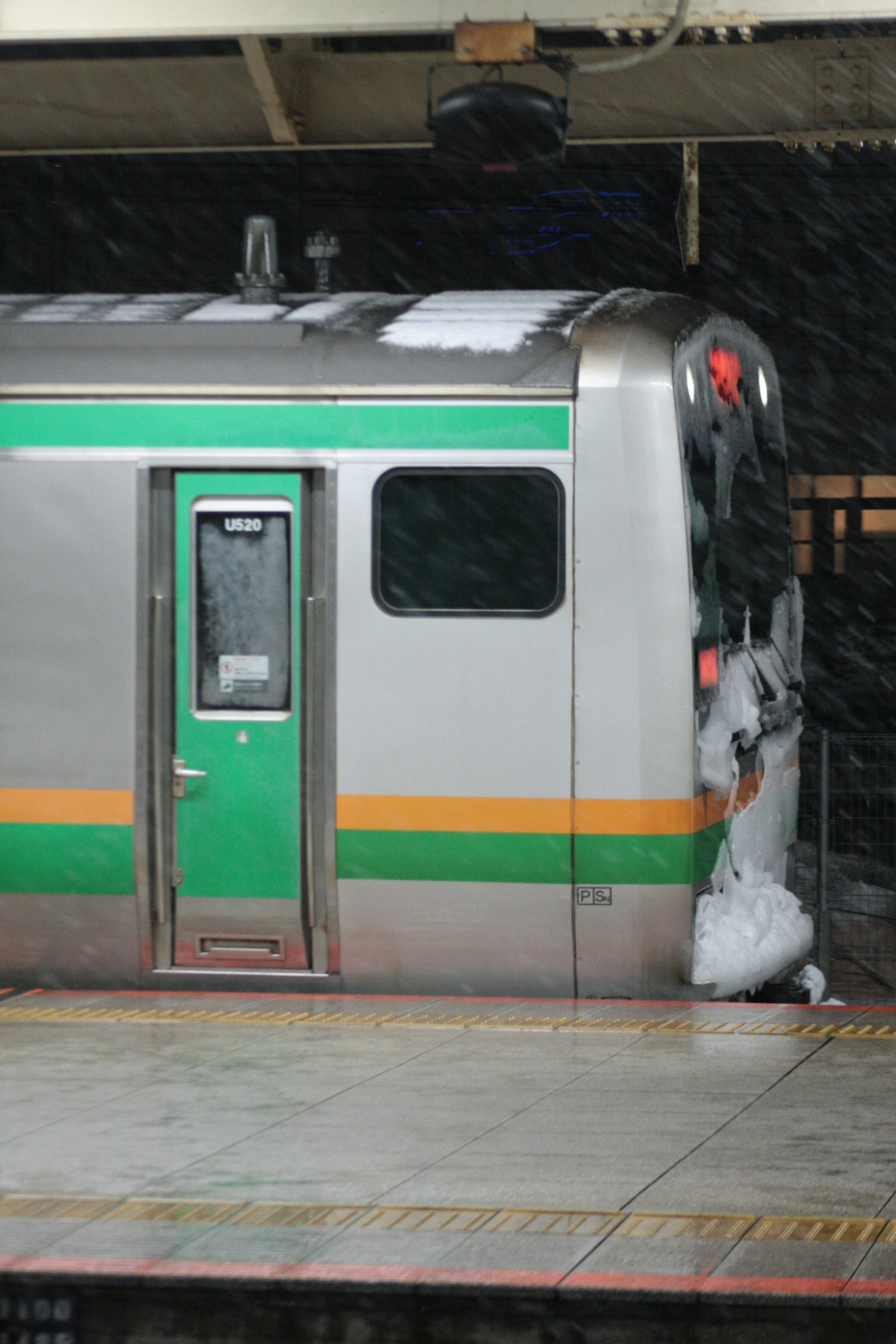 Vista lateral de un tren cubierto de nieve con franjas verdes y naranjas