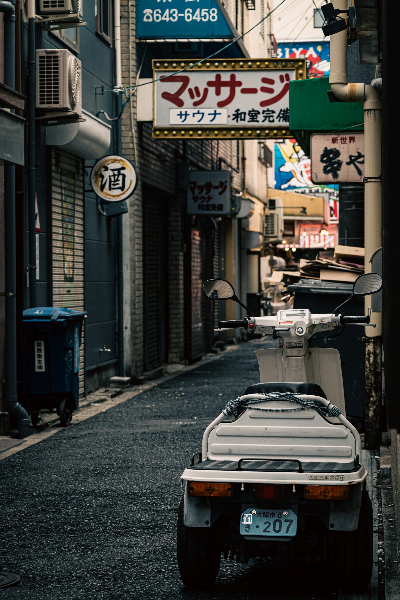 狭い路地に停まった白いバイクと日本の看板が並ぶ風景