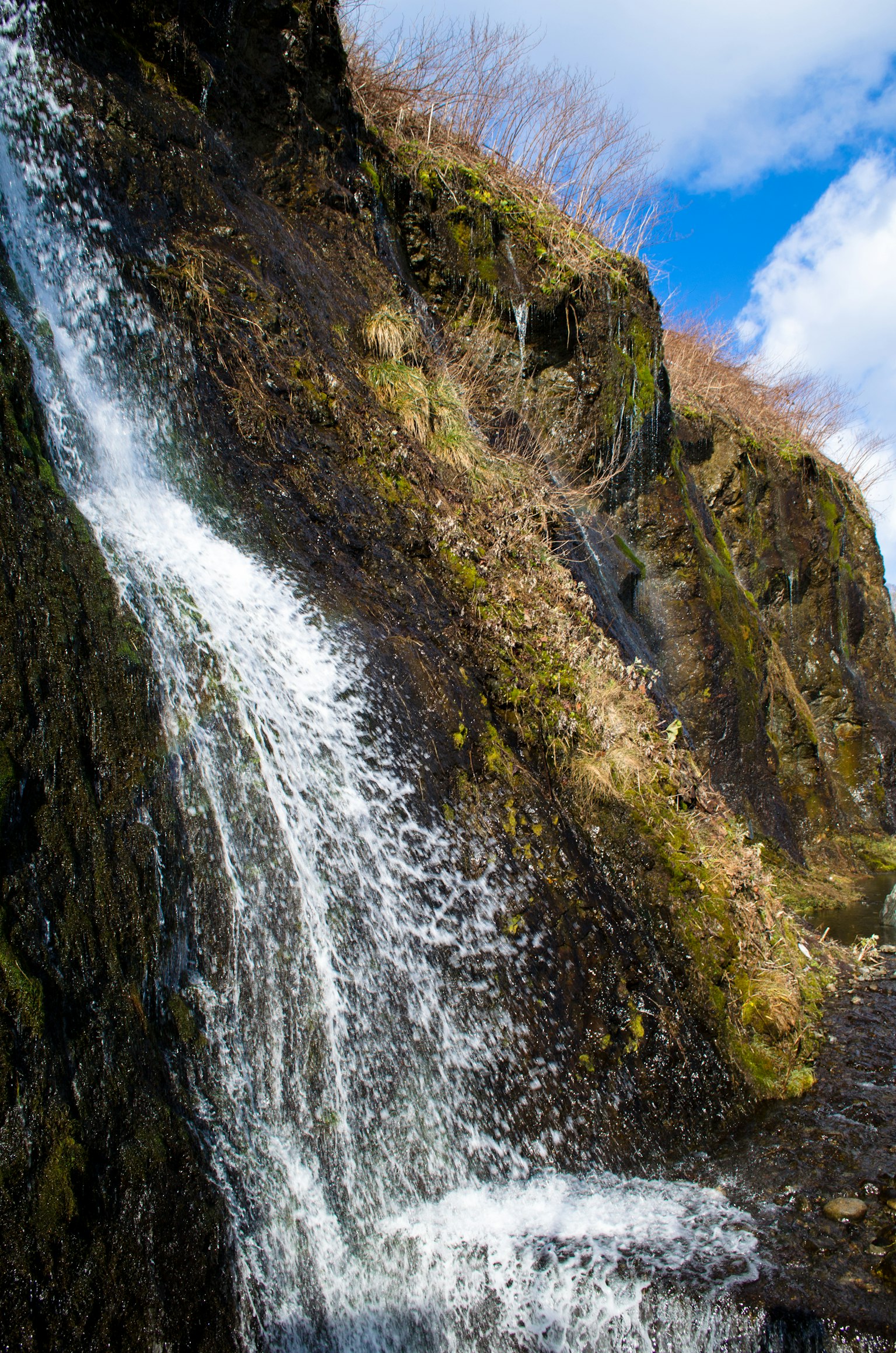 Cascada fluyendo sobre rocas cubiertas de musgo bajo un cielo azul