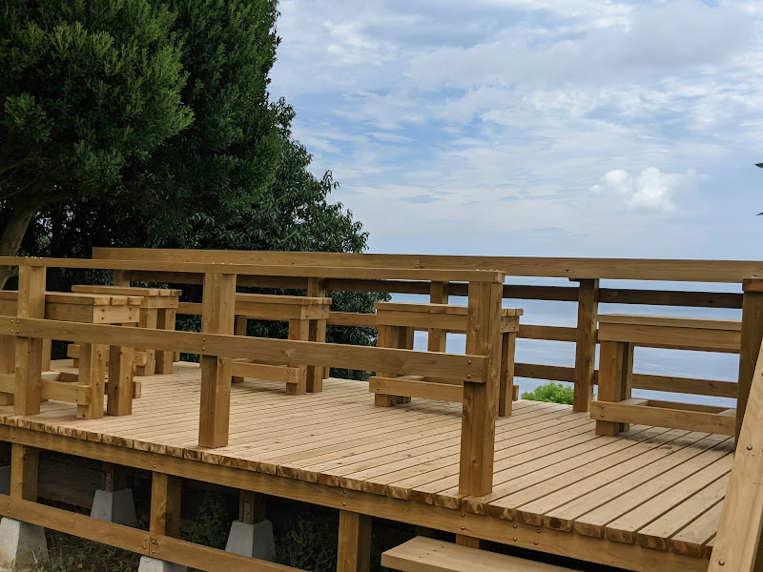 Terrasse en bois surplombant la mer avec des arbres en arrière-plan
