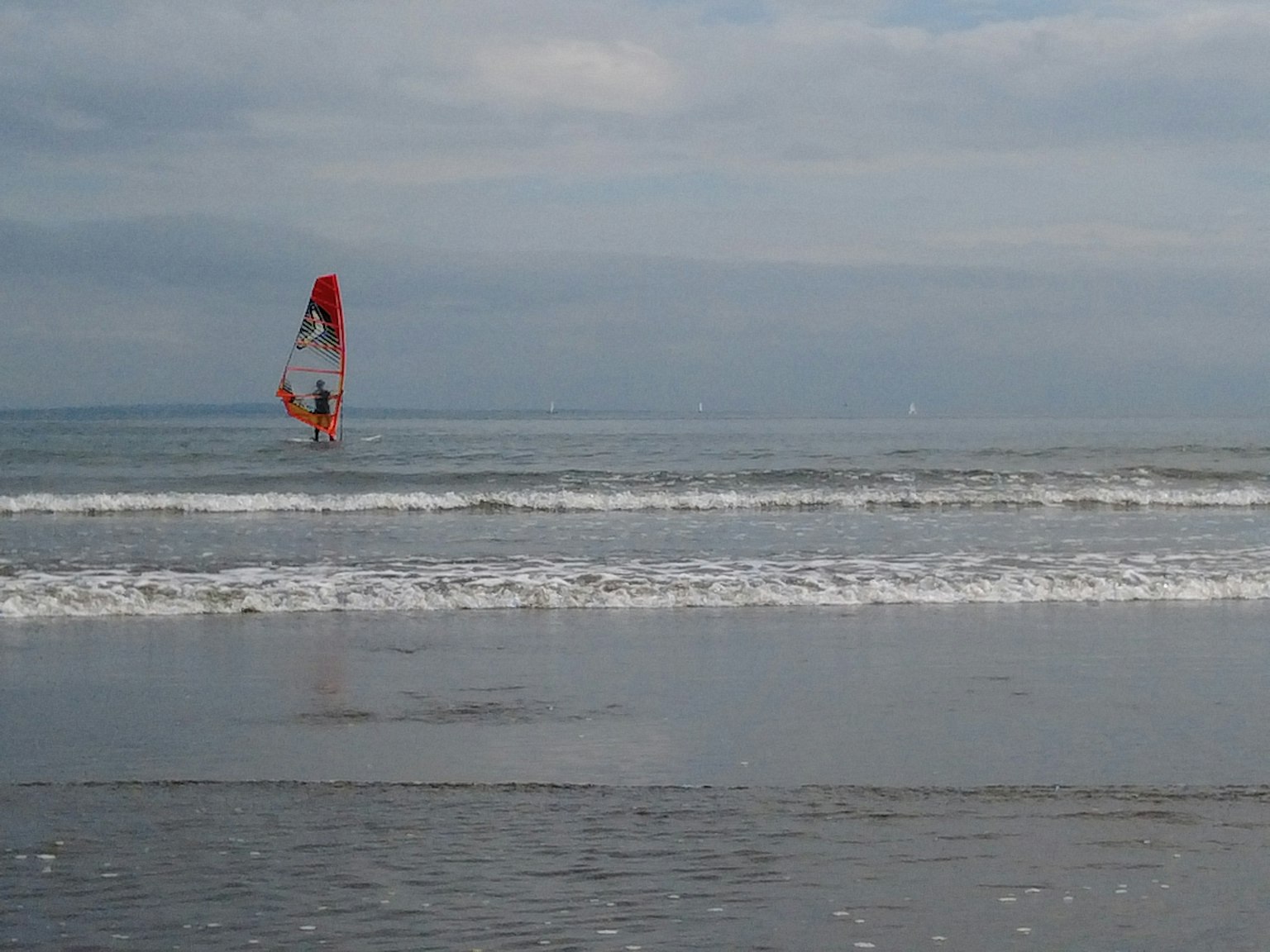 Persona haciendo windsurf en el océano con una vela roja y olas tranquilas