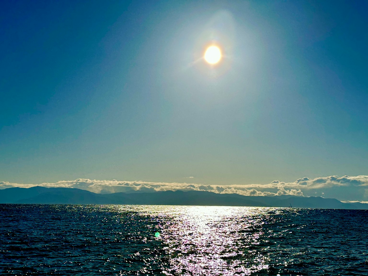 Sol brillante sobre un océano reluciente con montañas a lo lejos