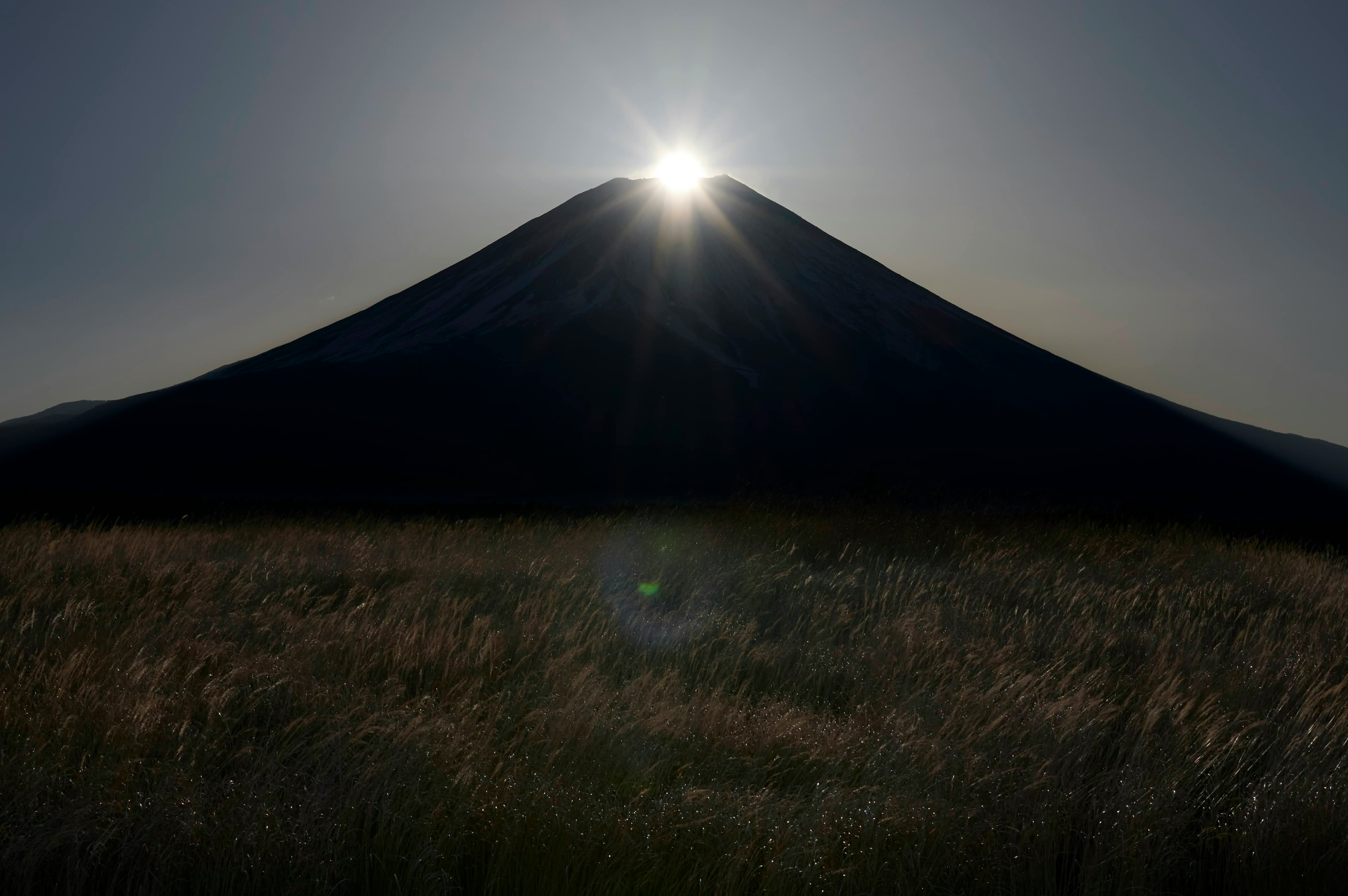 草原の向こうにそびえる山と朝日の光芒