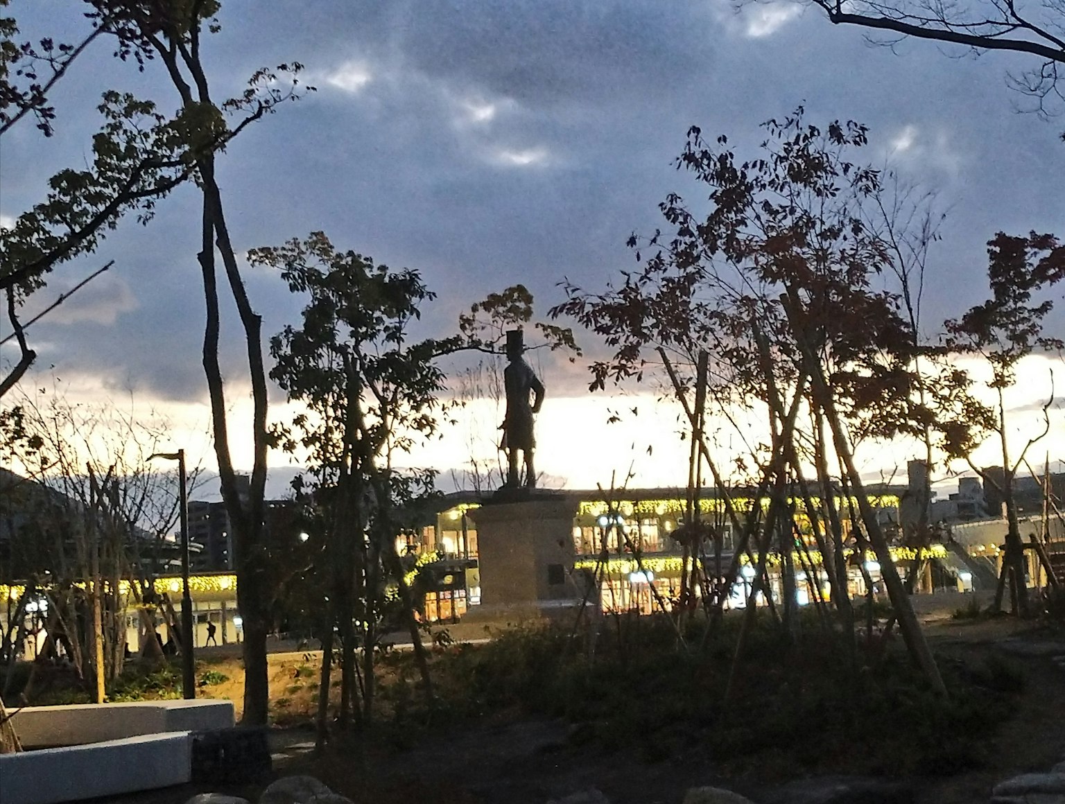 Estatua en un parque al anochecer rodeada de árboles