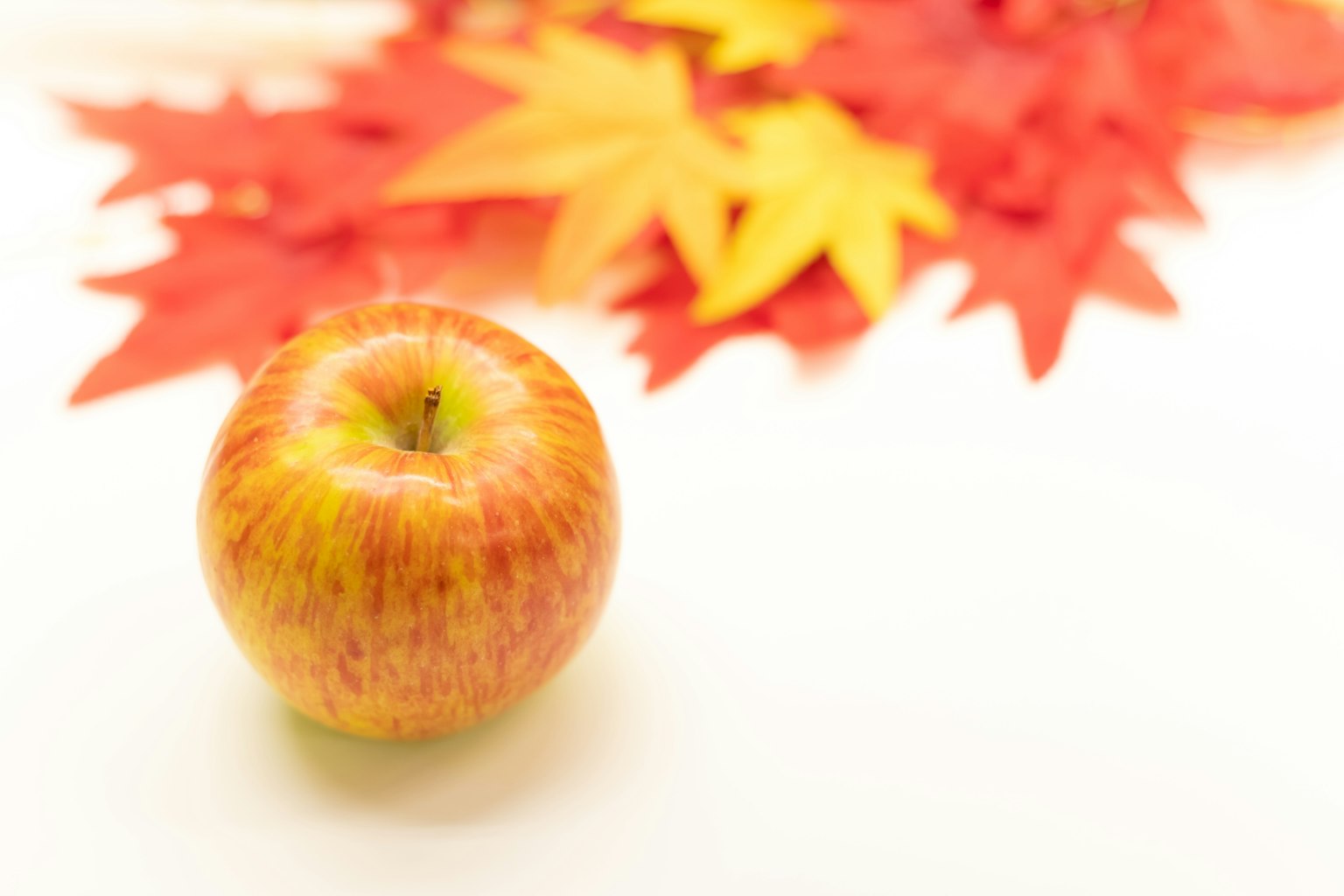 Une pomme rouge devant des feuilles d'automne colorées
