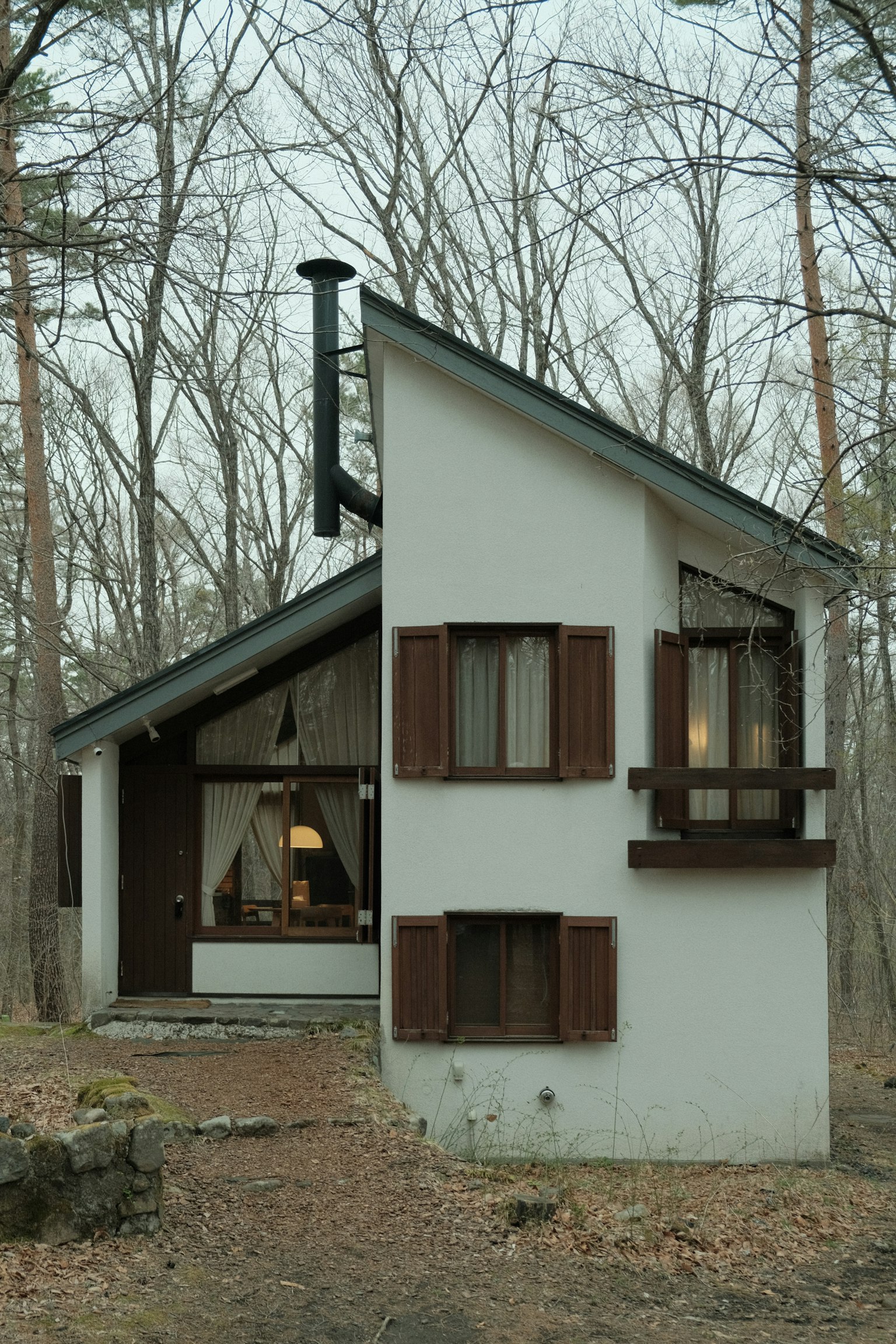 Casa bianca unica che si erge tra gli alberi con finestre e persiane distintive