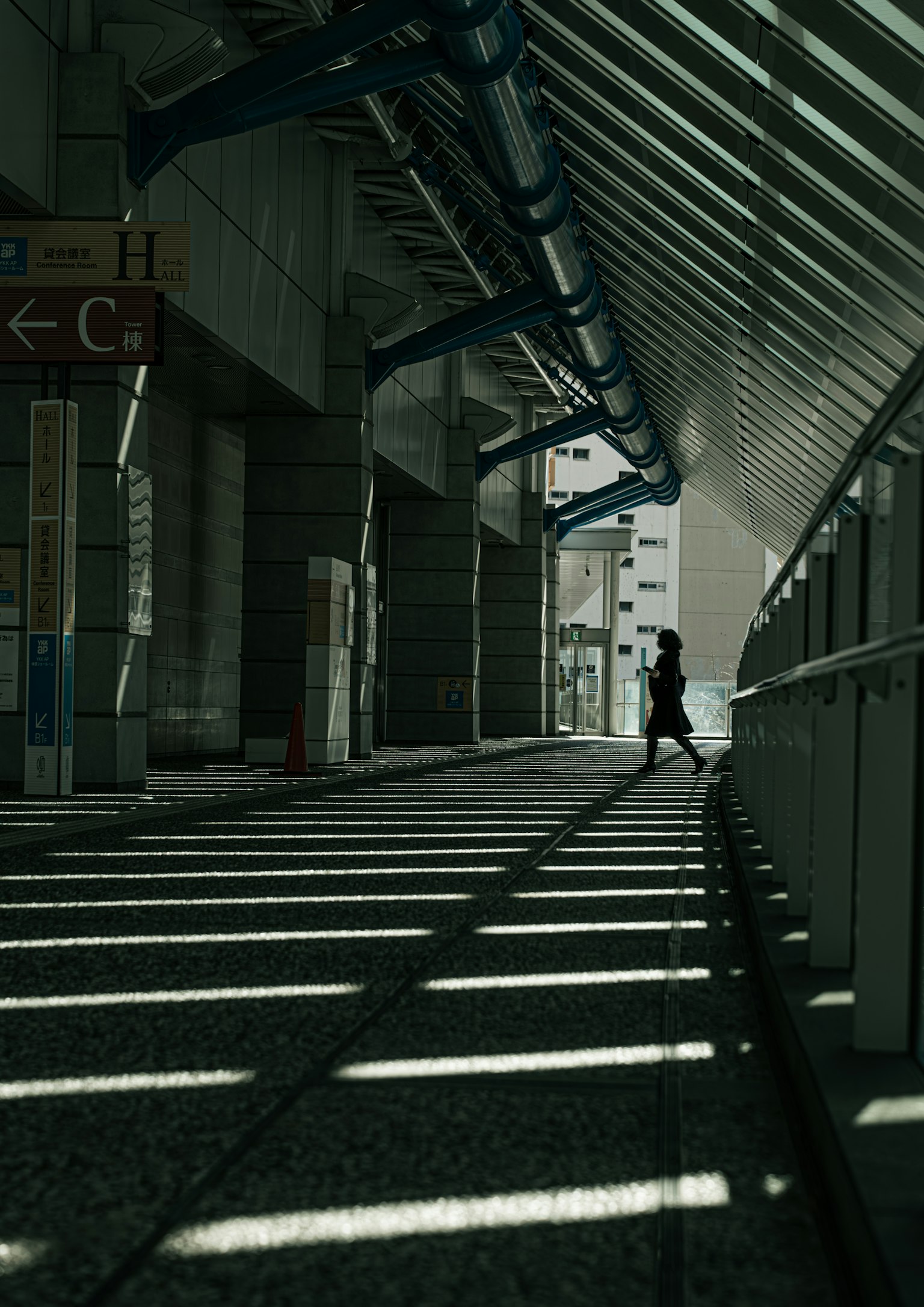 A person walking through a modern corridor with striking shadow stripes