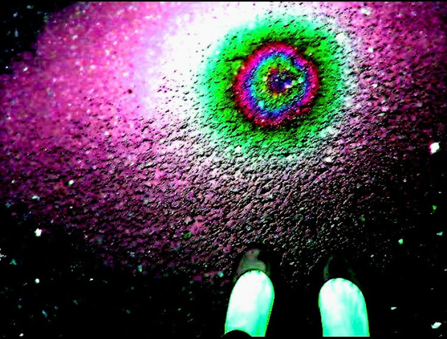 A vibrant swirl pattern in bright colors on the ground with shoes positioned in front of it