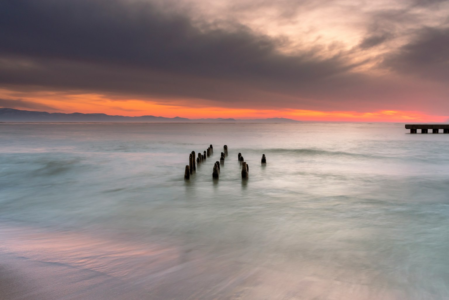 Meereslandschaft mit einem versunkenen Pier und lebhaftem Sonnenuntergang