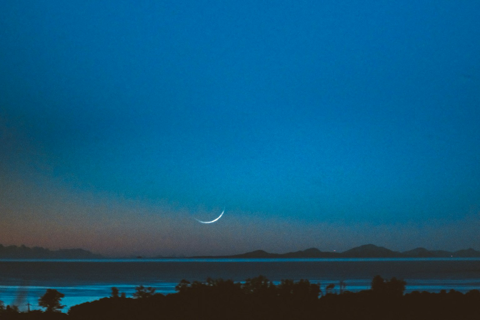 Langit malam biru dengan bulan sabit dan pemandangan laut