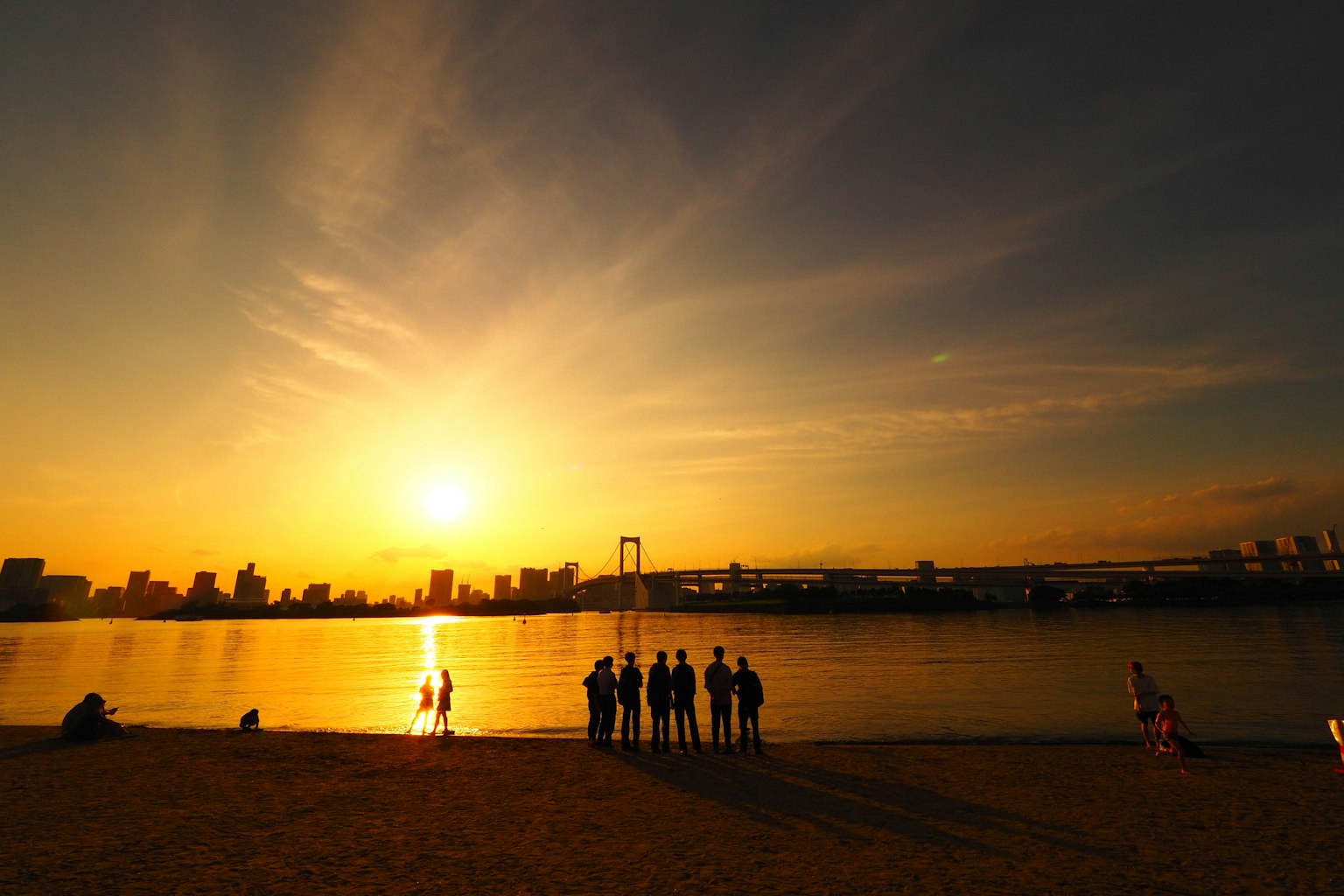 เงาของผู้คนที่ชายทะเลกับพระอาทิตย์ตกและเส้นขอบฟ้าของเมือง