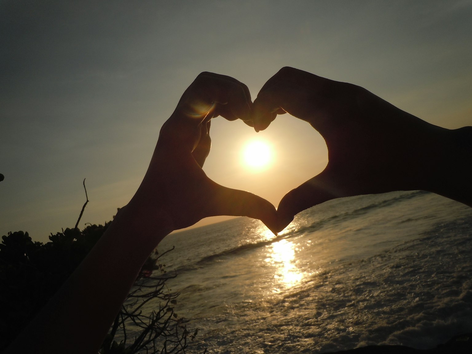 Hände formen ein Herz gegen einen Sonnenuntergang