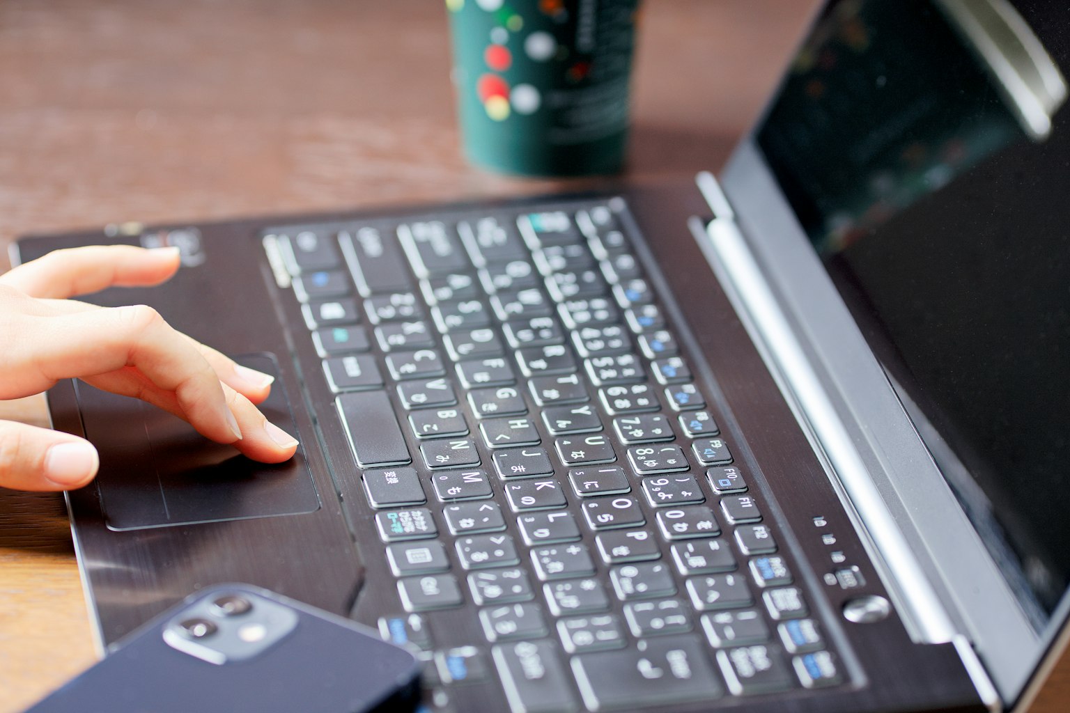 Eine Hand tippt auf die Tastatur eines Laptops mit einer Kaffeetasse und einem Smartphone in der Nähe